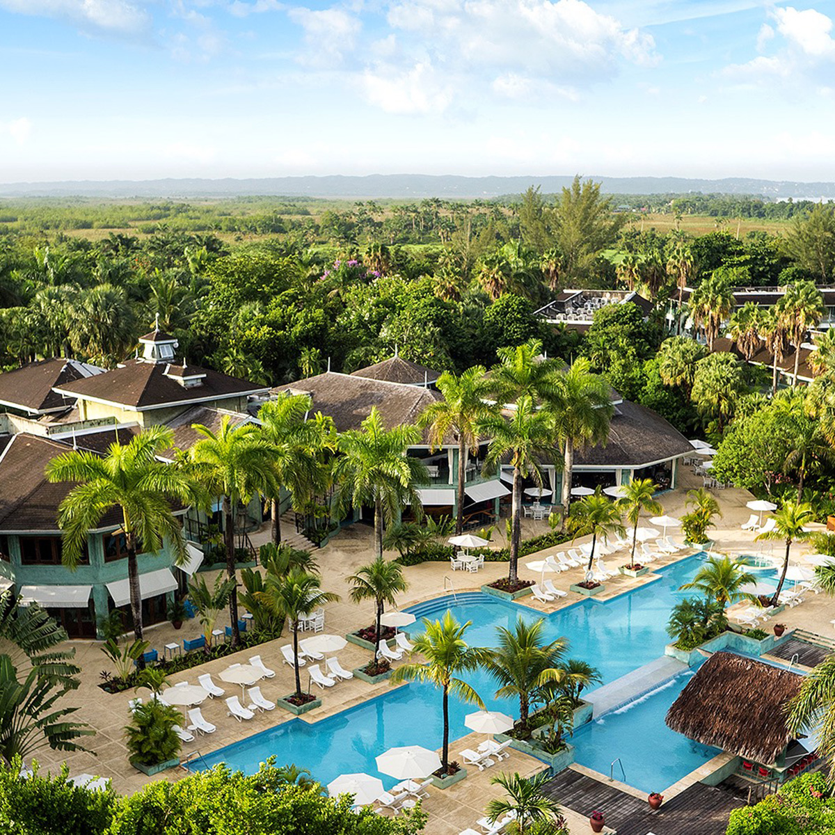 Aerial view of Couples Negril resort with swimming pools surrounded by palm trees.