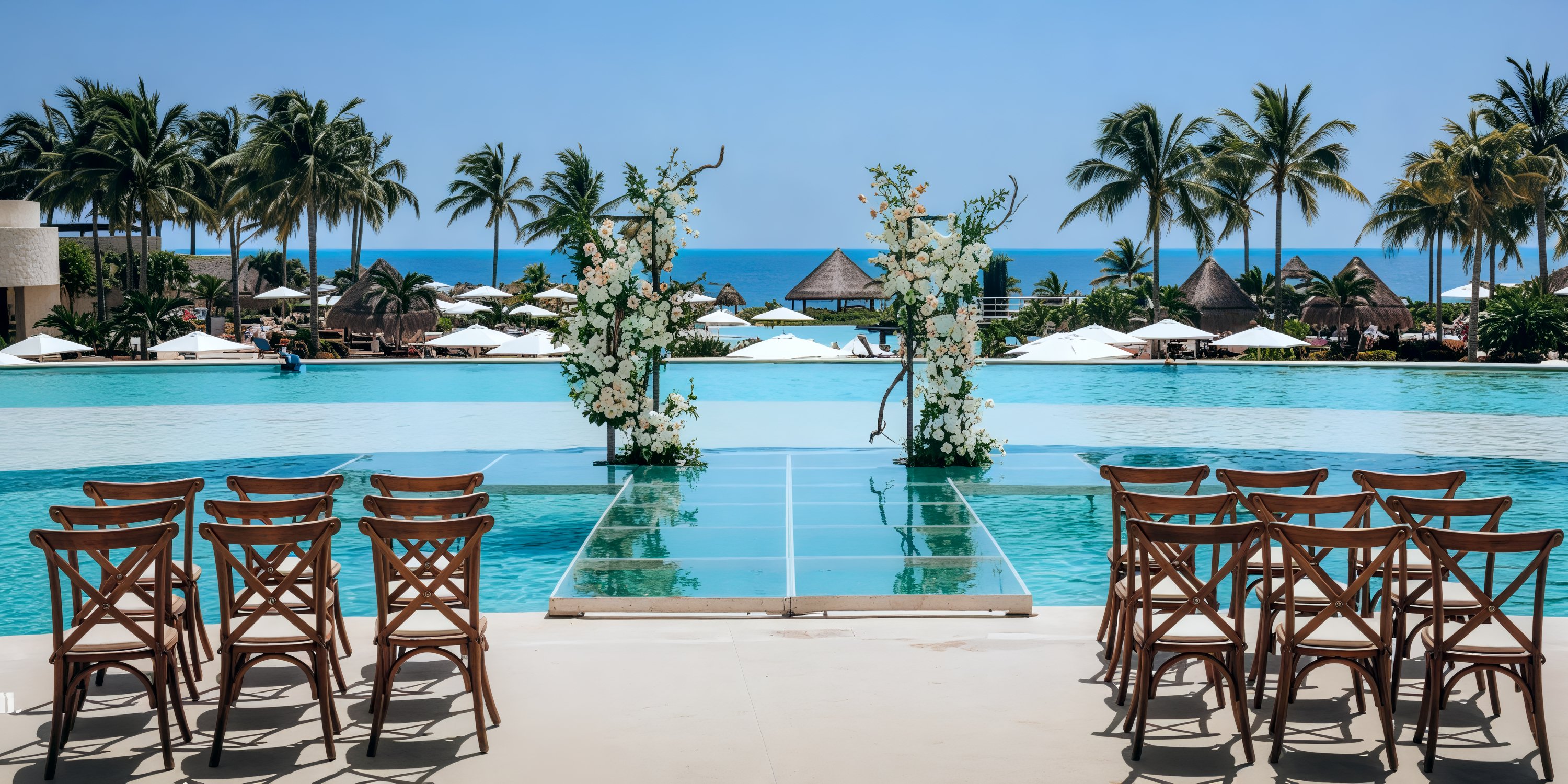 Destination wedding arranged in a tropical outdoor setting, featuring a poolside view adorned with palm trees and overlooking the ocean.