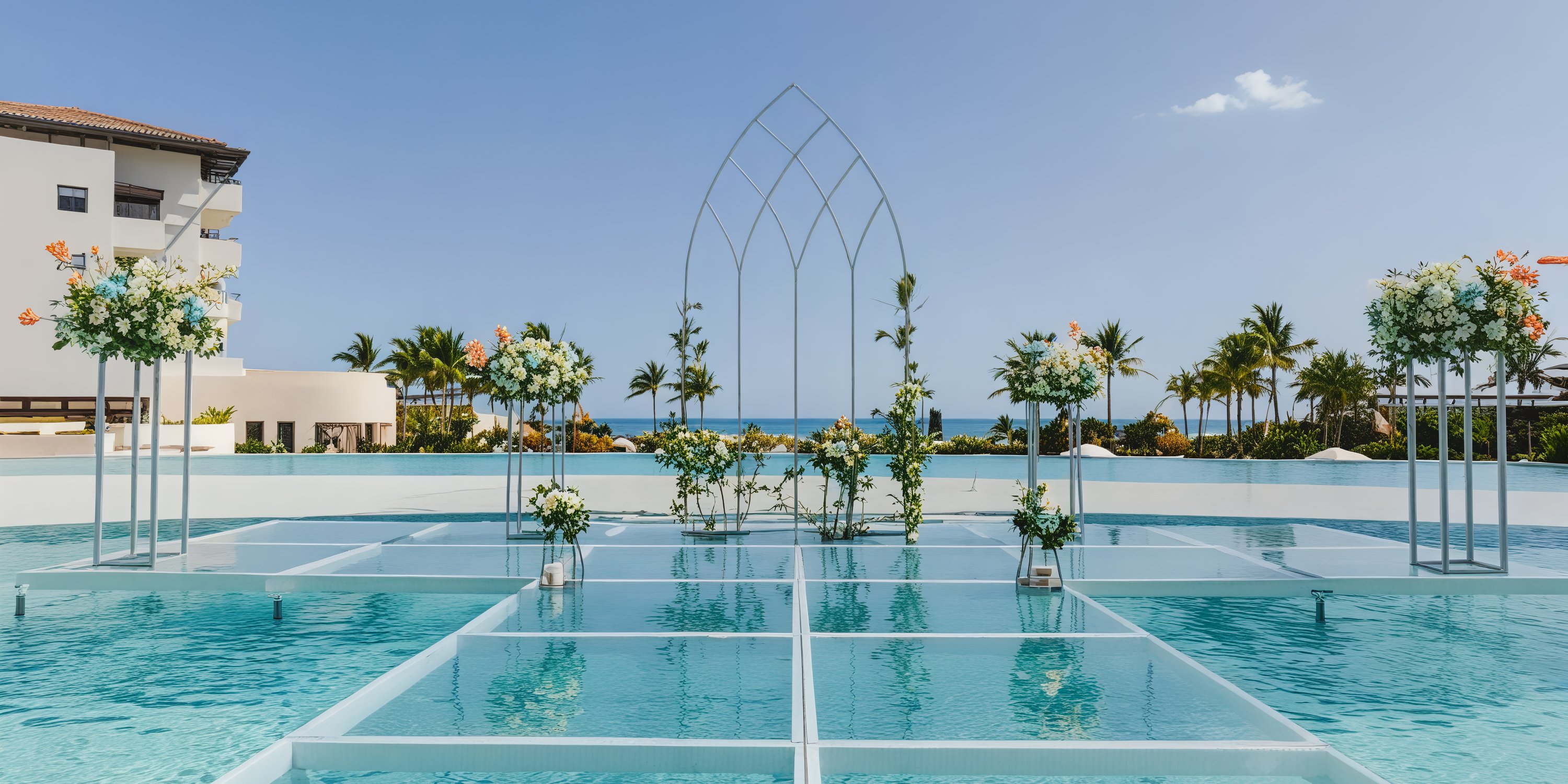 An exquisite destination wedding arrangement featuring a floral-adorned glass platform elegantly poised over a pool, all set against the breathtaking backdrop of the ocean.