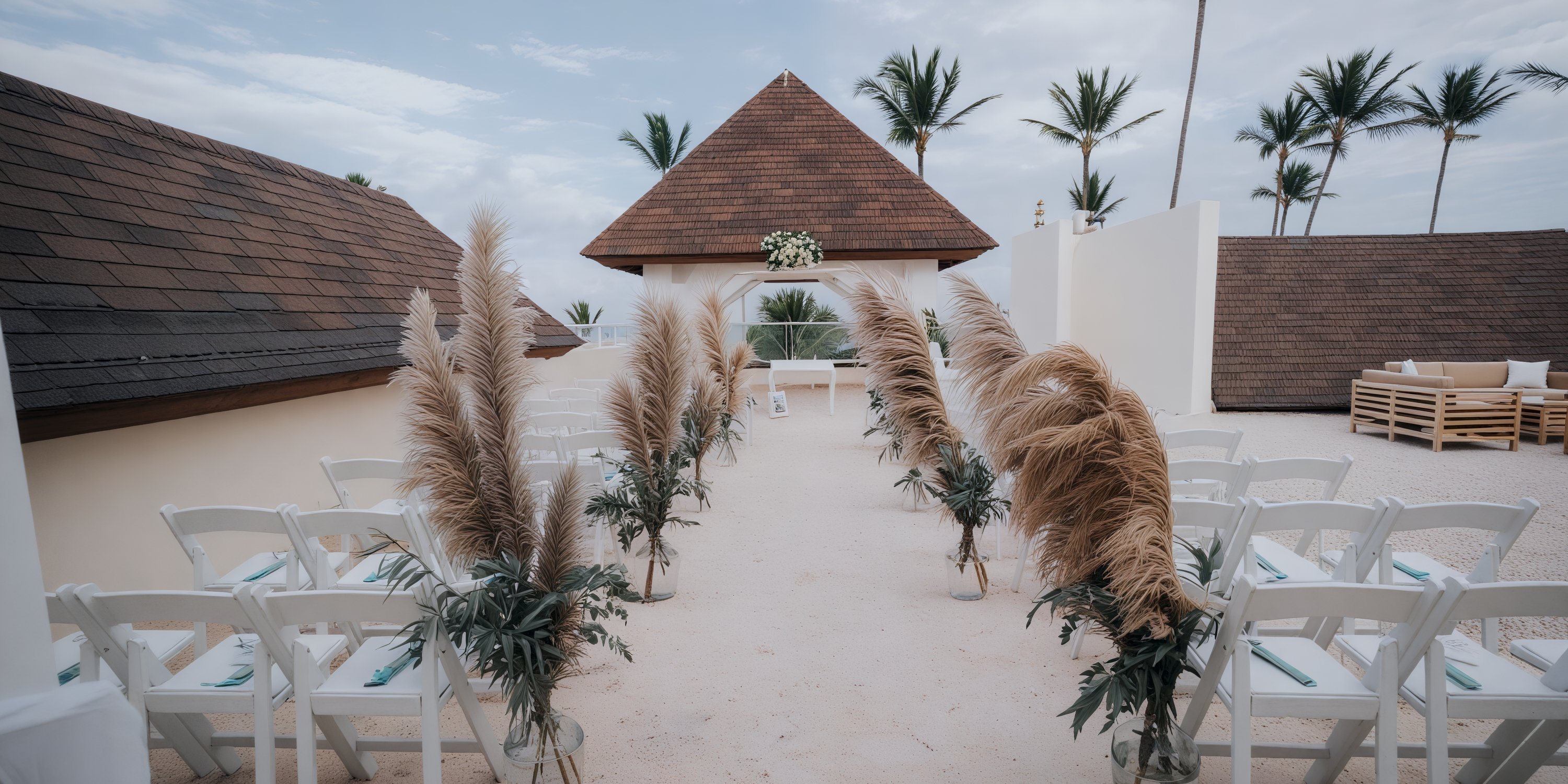 A beautifully arranged aisle at Dreams Royal Beach, adorned with pampas and wooden chairs, elegantly facing the wedding altar—perfect for a romantic destination wedding.