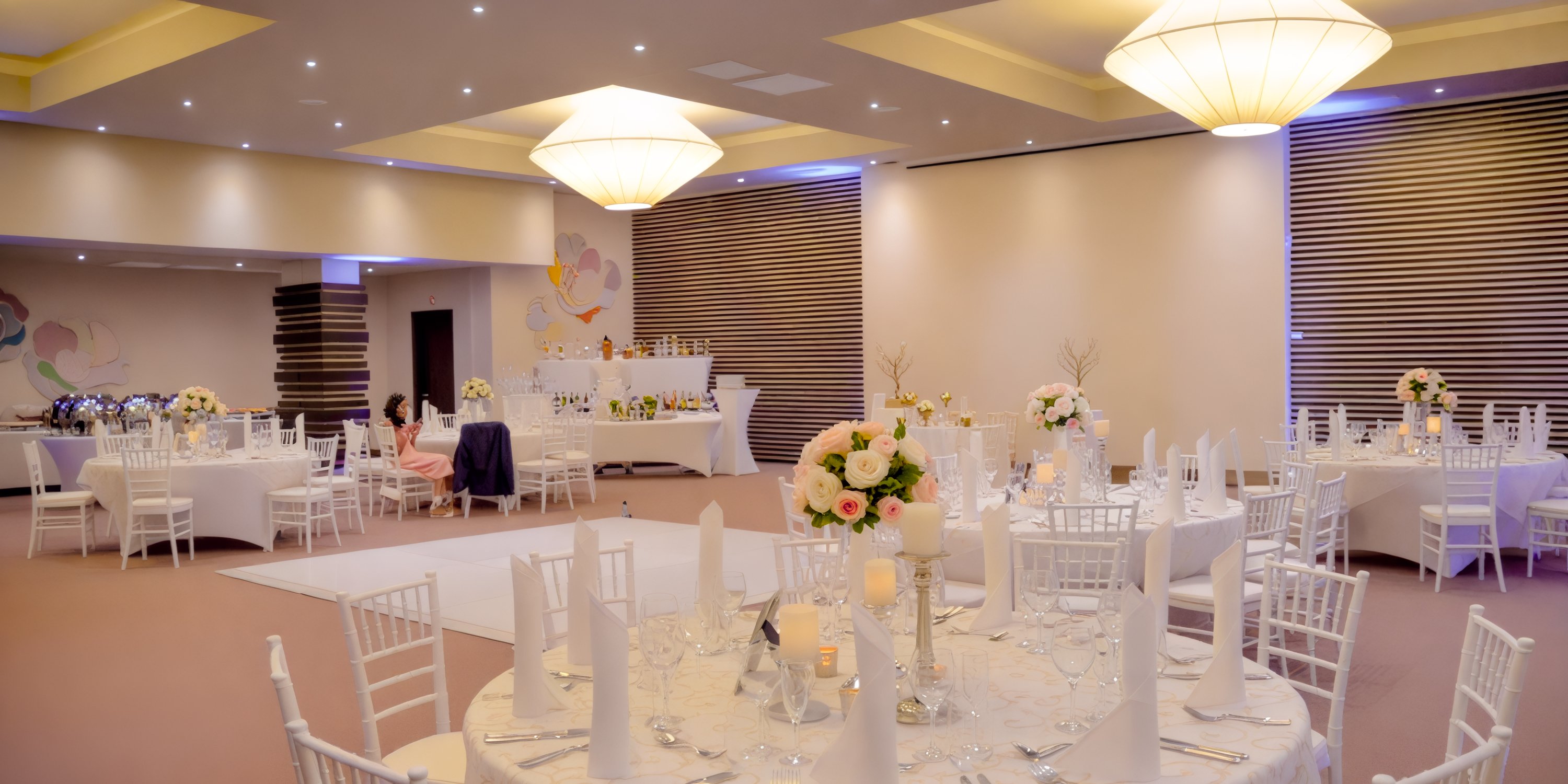 Dreams Onyx offers an exquisite setup for a destination wedding, featuring round tables adorned with elegant floral centerpieces and complemented by white chairs, all within a sophisticated banquet hall setting.
