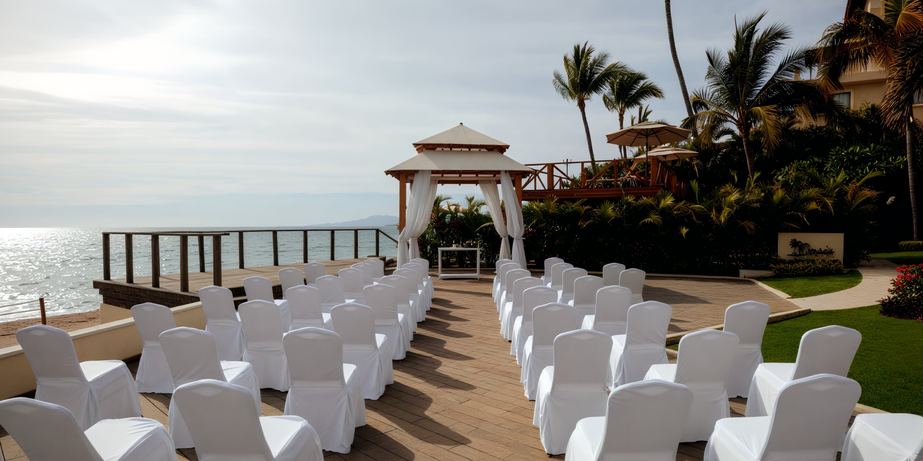 Experience the idyllic destination wedding at Dreams Vallarta Bay, where the oceanfront ceremony features chairs perfectly positioned towards the altar and elegantly framed by swaying palm trees.