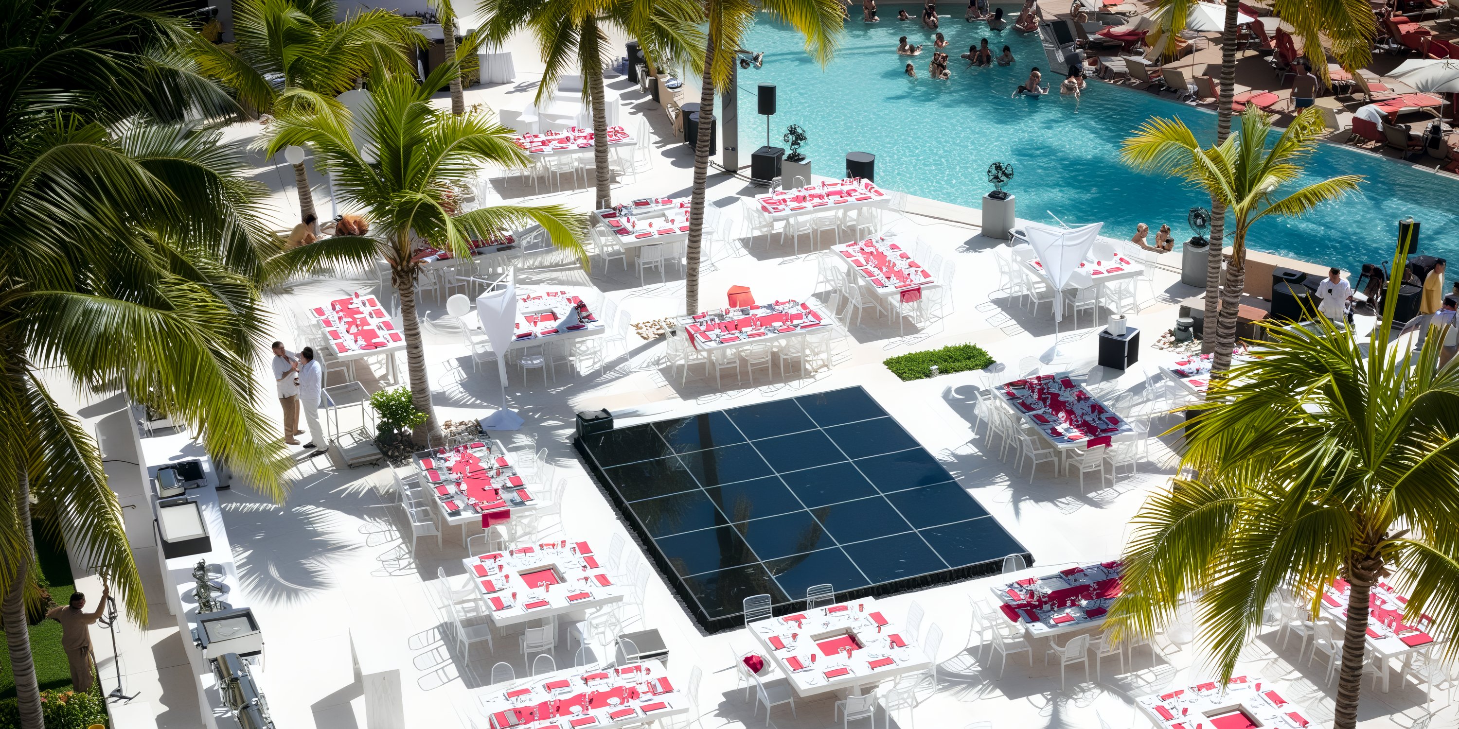 Dreams Vallarta Bay provides a picturesque poolside setup perfect for a destination wedding, featuring elegantly arranged tables adorned with red decor. Surrounded by swaying palm trees and the joyful scene of swimming guests, it creates an unforgettable backdrop for your special day.