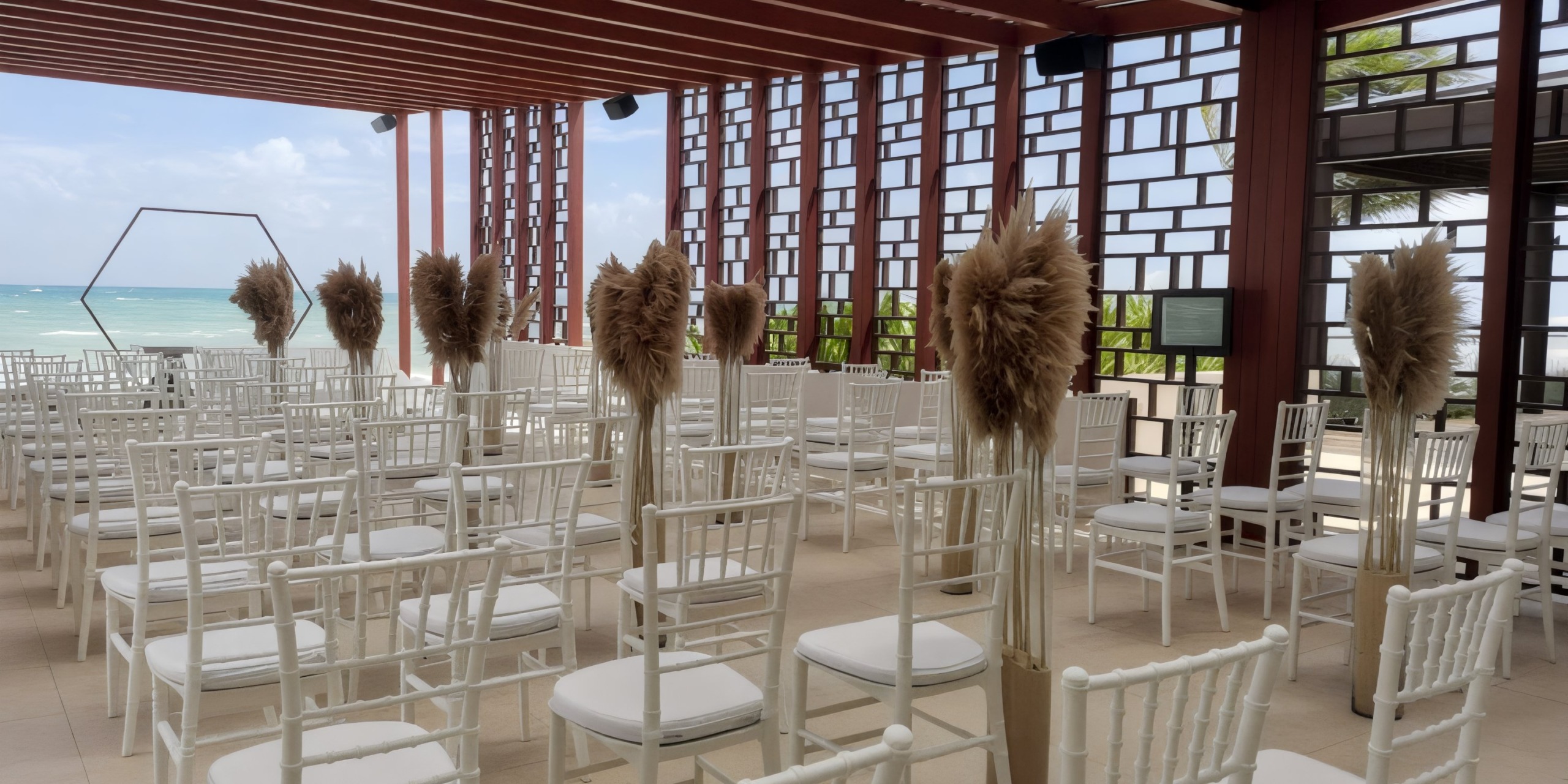 An outdoor destination wedding venue at Dreams Jade Riviera Cancun features elegant white chairs, pampas grass decor, and breathtaking ocean views.