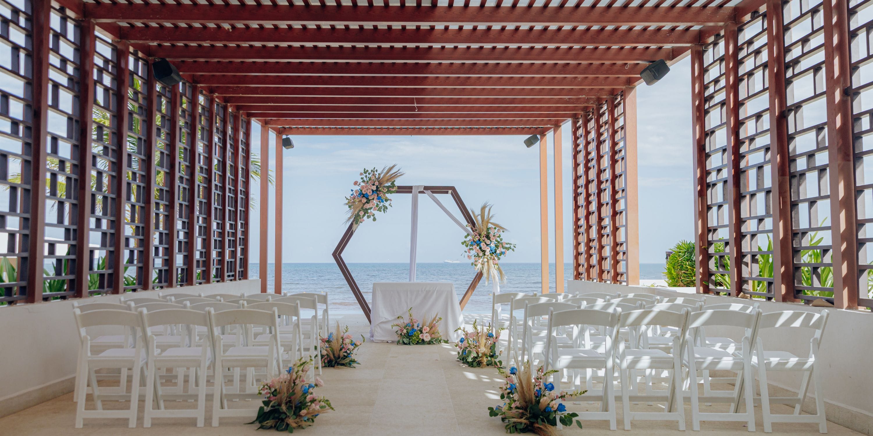 Destination wedding at Dreams Jade Riviera Cancun with white chairs, floral decor, and an ocean view.