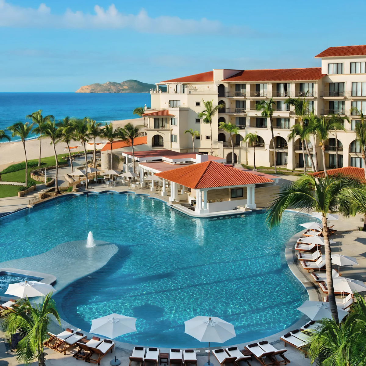 Luxury Dreams Los Cabos beachfront resort, perfect for a destination wedding, with a large swimming pool, sun loungers, and palm trees, overlooking the ocean.