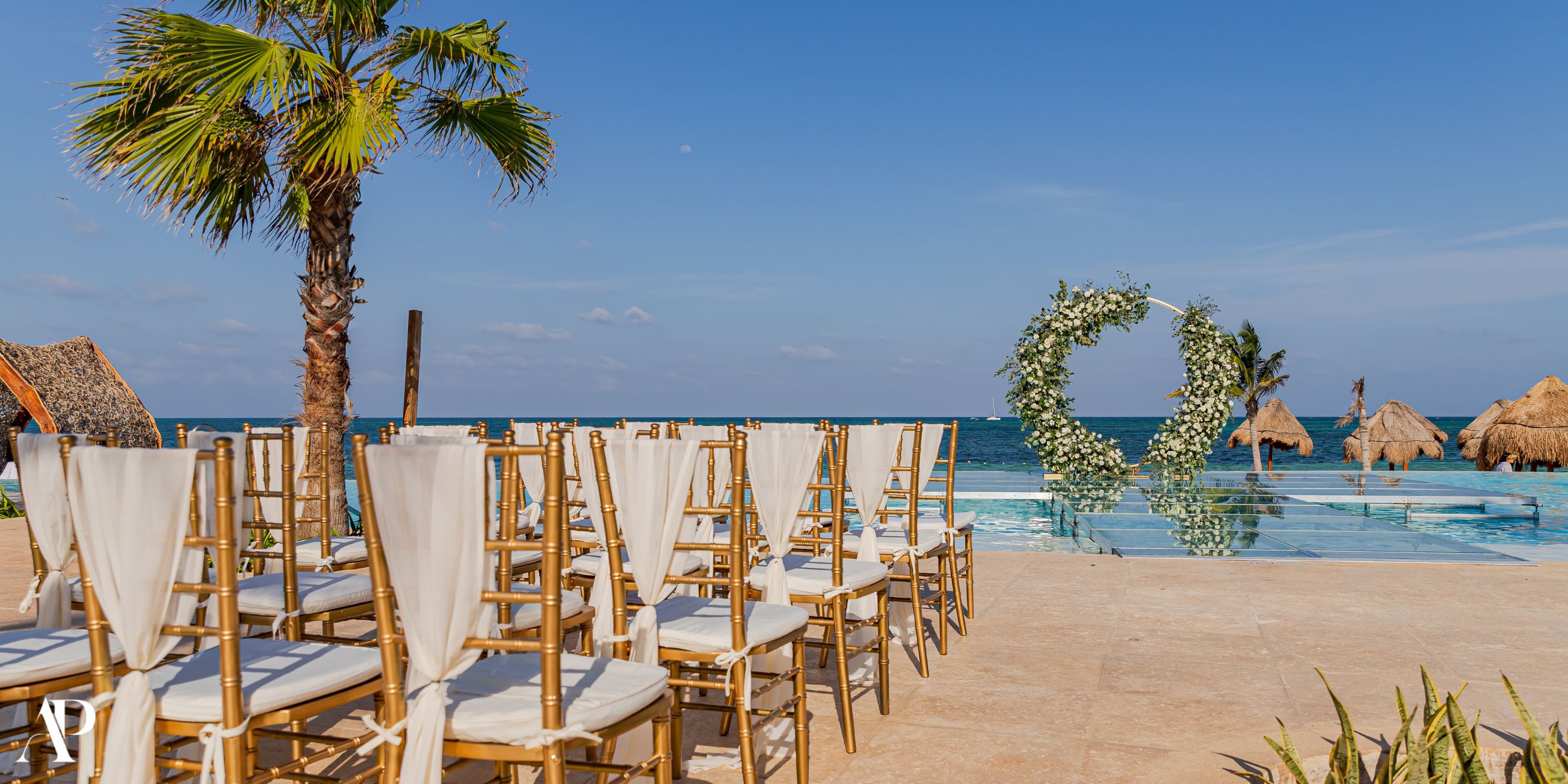 Dreams Natura destination wedding setup: oceanfront chairs, floral arch, and sunny blue skies.