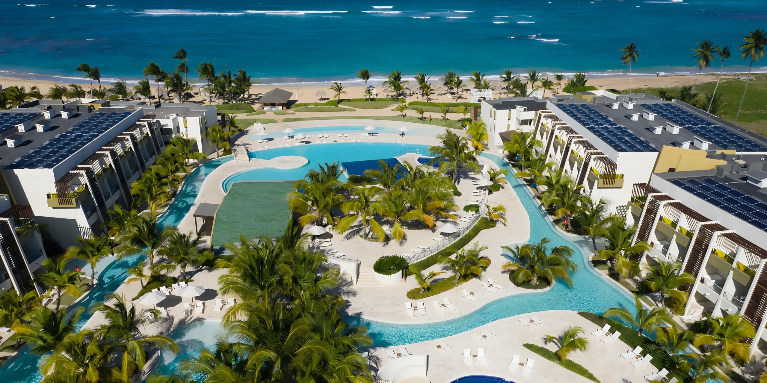 Aerial view of Dreams Onyx, a luxury beachfront resort with large swimming pools surrounded by palm trees, adjacent to a sandy beach and turquoise sea.