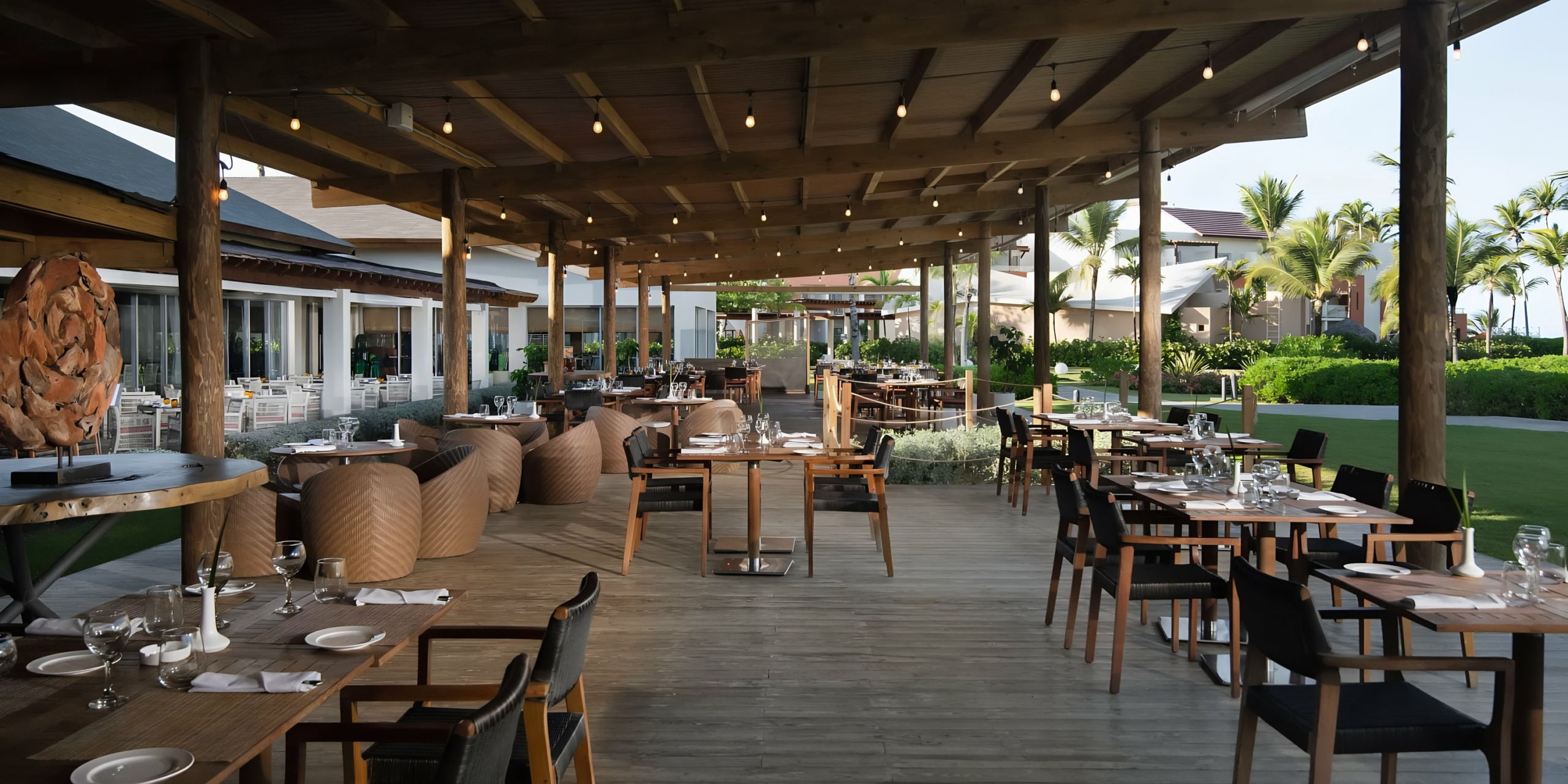 Outdoor restaurant with Dreams Onyx flooring and furniture, set tables, under a covered patio area extending into a landscaped garden.
