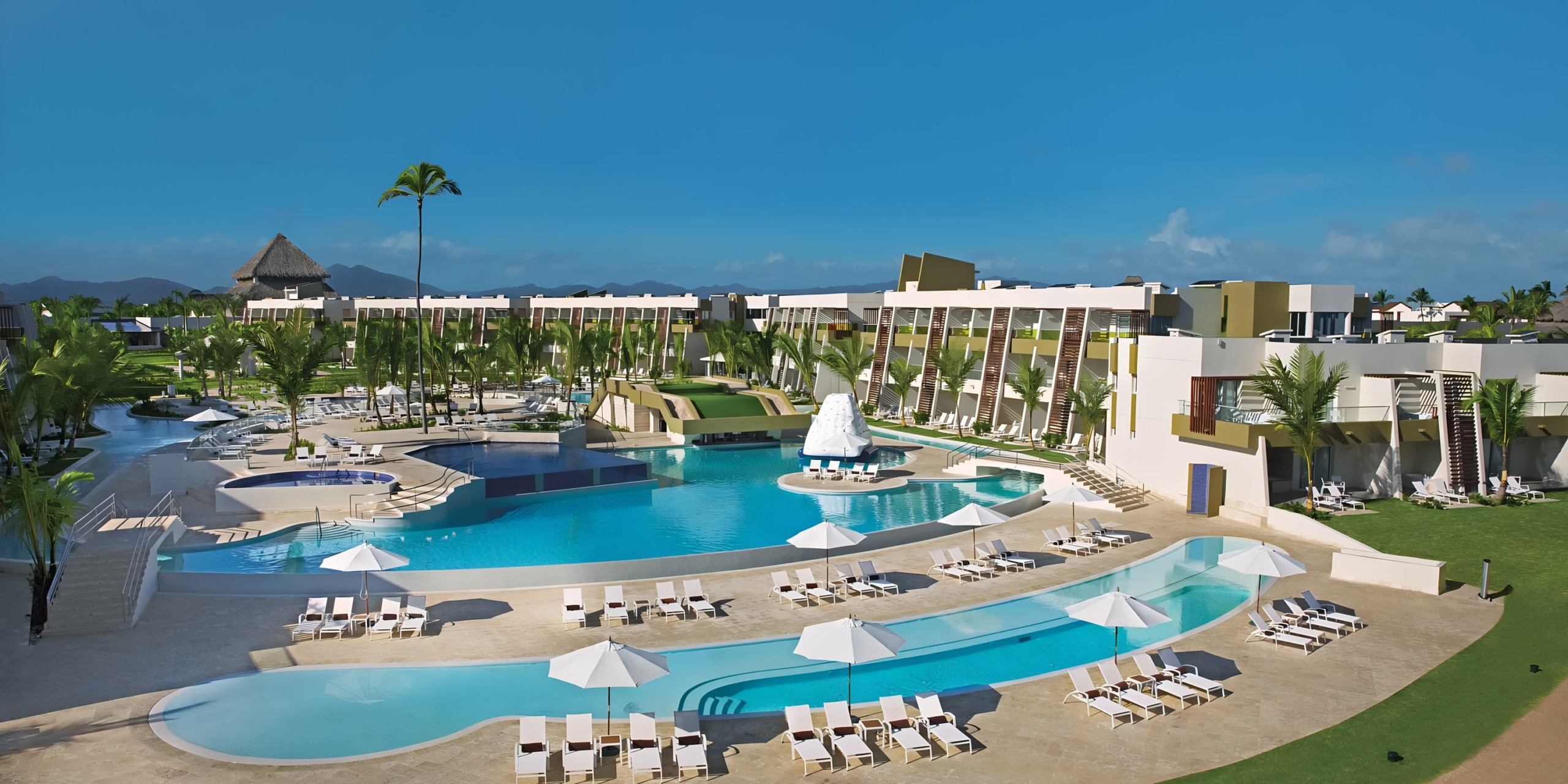 A Dreams Onyx resort with large swimming pools, loungers, palm trees, and modern buildings under a clear blue sky.