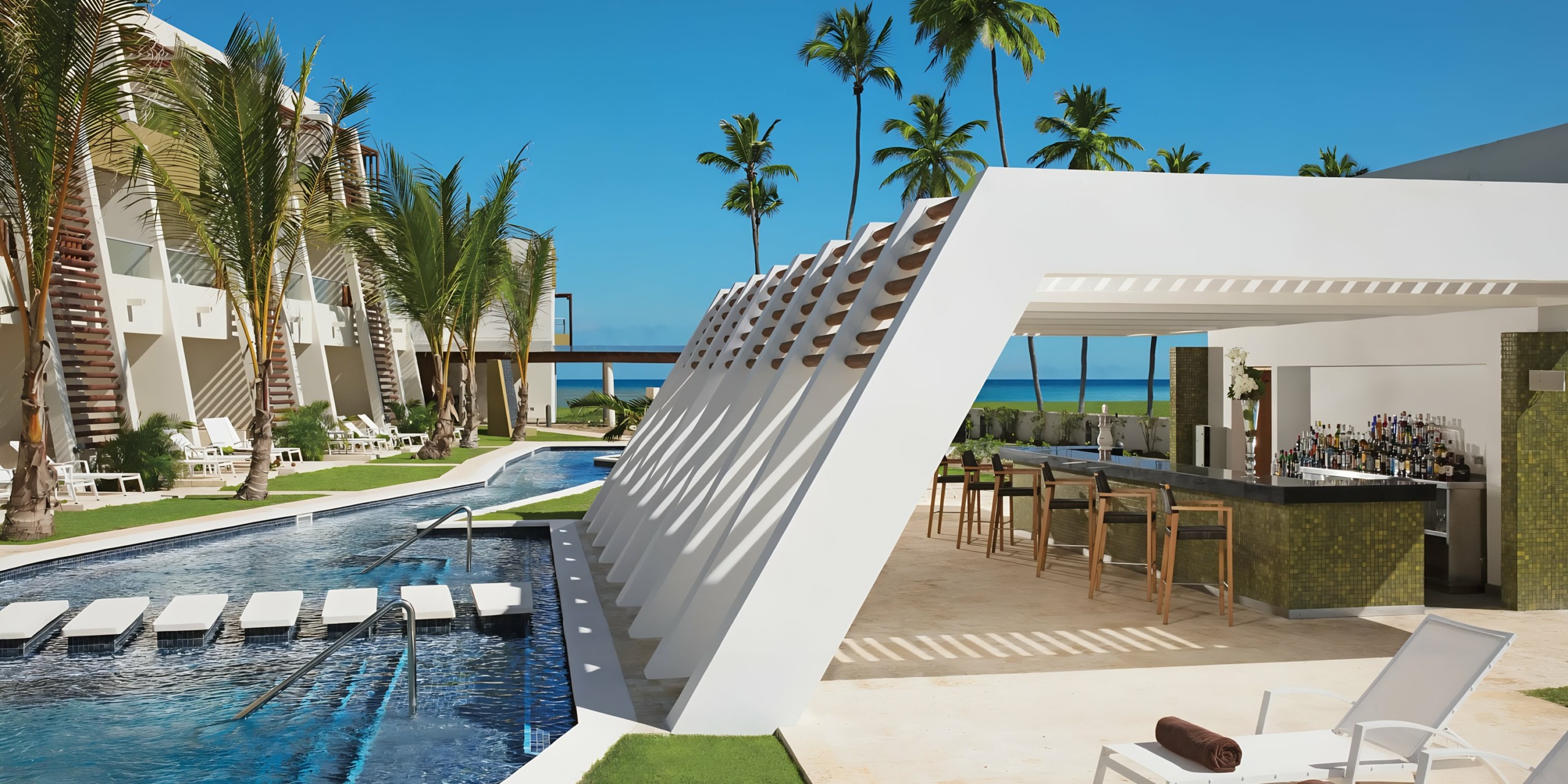 A Dreams Onyx resort pool with a swim-up bar surrounded by palm trees, white sun loungers, and modern white buildings.