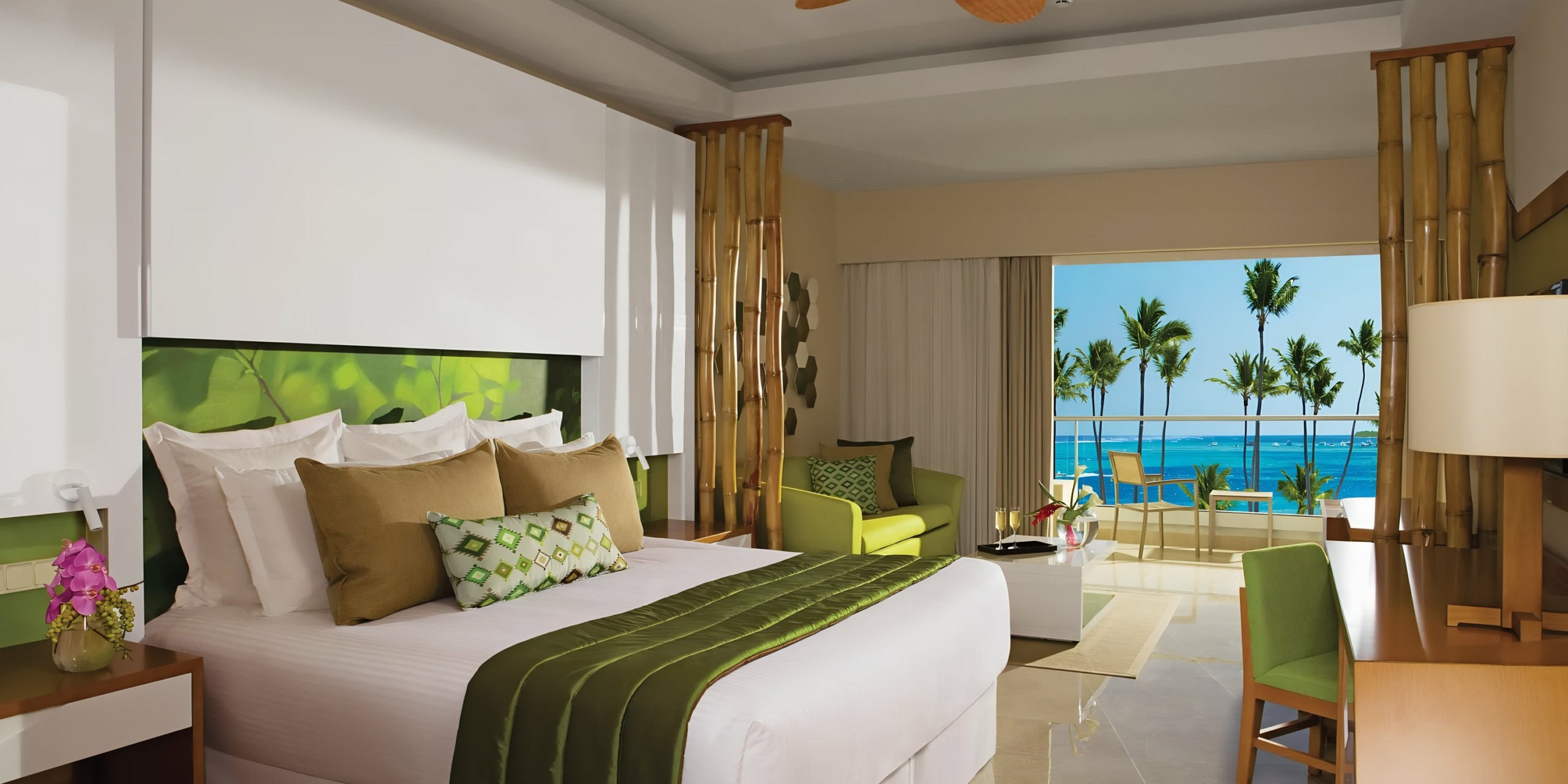 A luxurious Dreams Onyx hotel room with a large bed, green accents, and a balcony view of palm trees and the ocean.