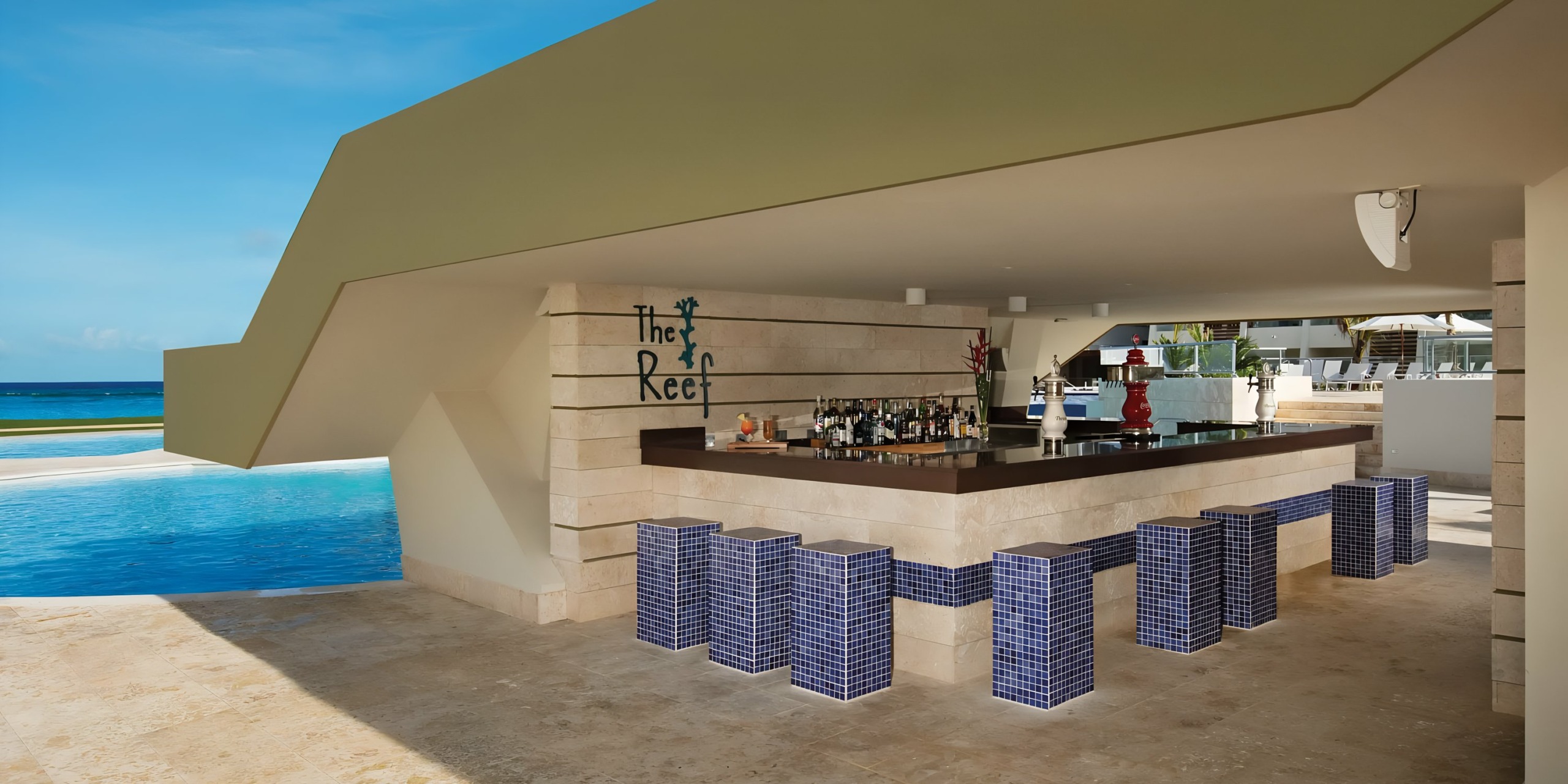 Outdoor bar named "Dreams Onyx" with a semi-circular design, featuring poolside seating and ocean view, under a large architectural overhang.