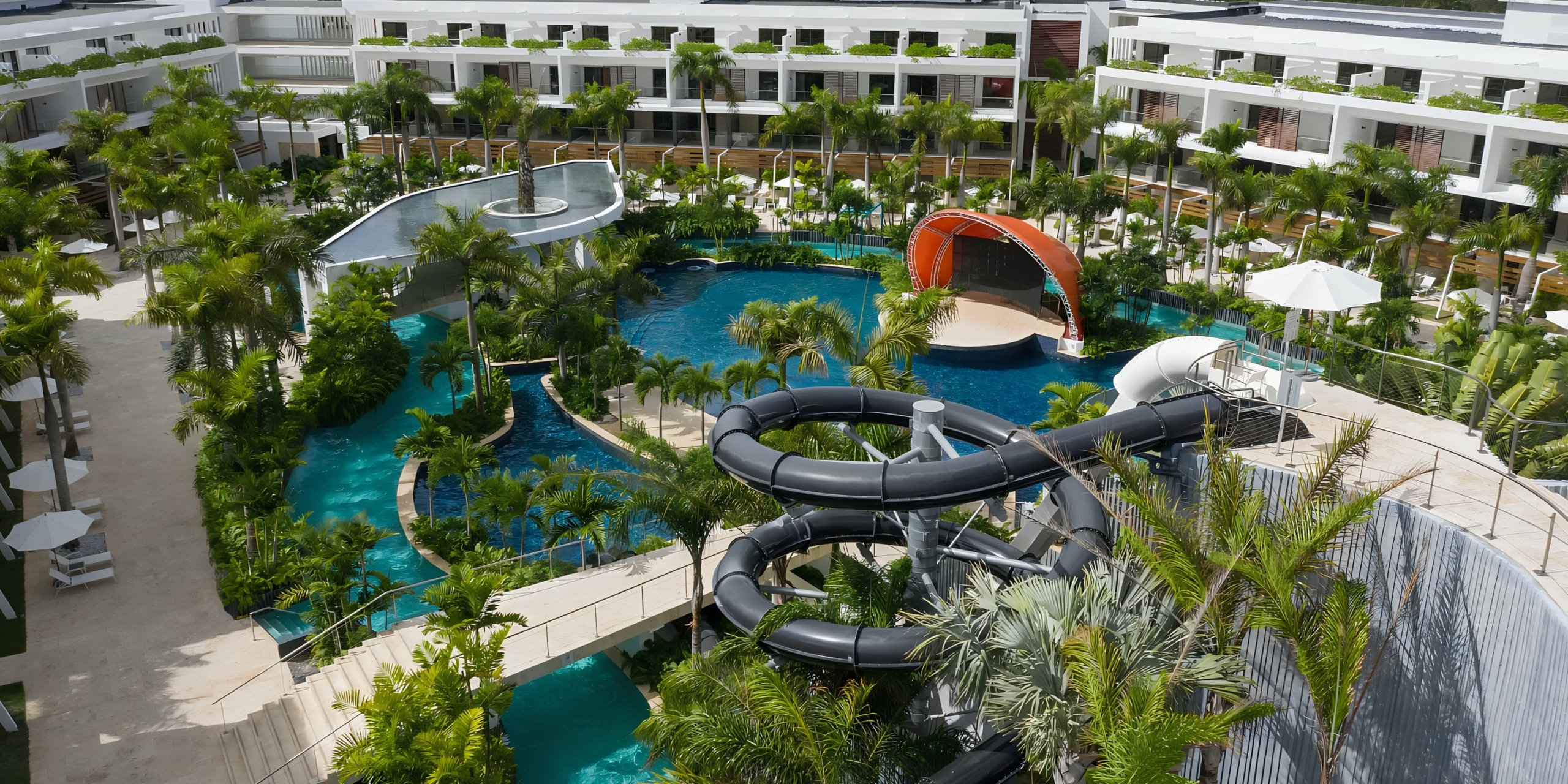 Aerial view of Dreams Onyx, a luxurious resort with a large tropical swimming pool complex, featuring winding water slides, surrounded by palm trees and modern white buildings.