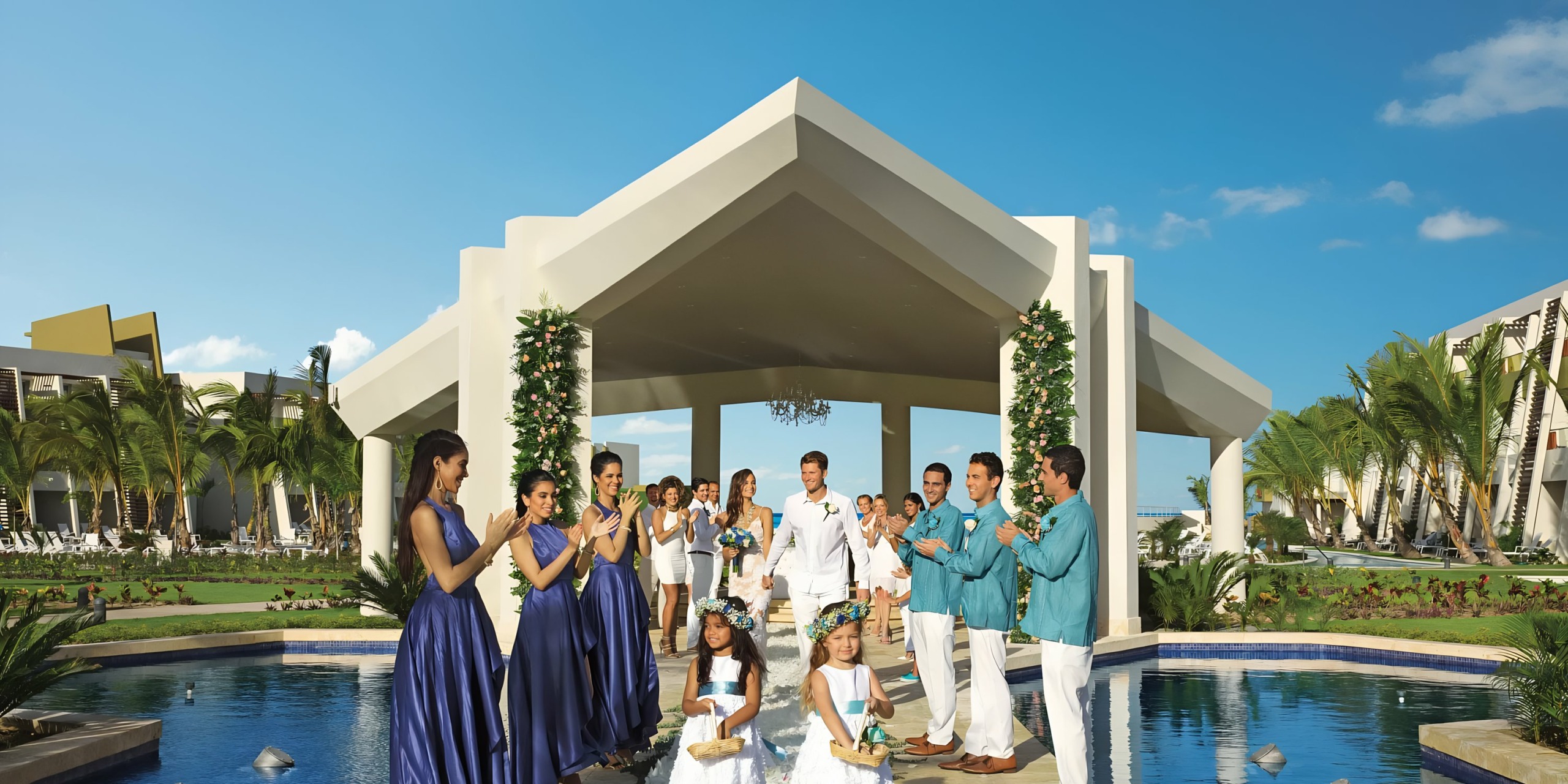 A Dreams Onyx wedding ceremony with a bride and groom, surrounded by bridesmaids and groomsmen, taking place at a modern outdoor venue by a pool.