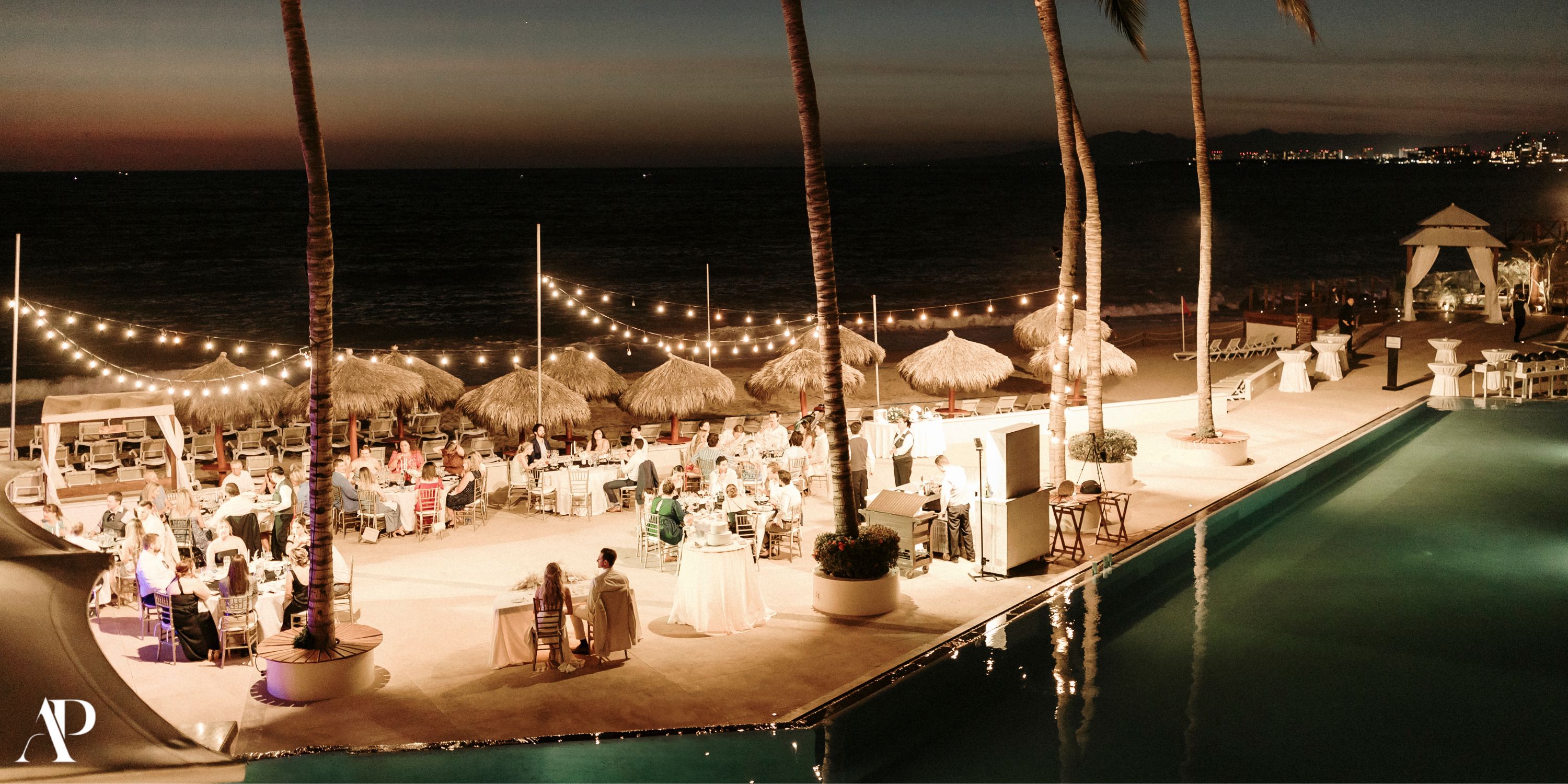 Destination wedding evening at Dreams Vallarta Bay with string lights, guests, tables, and ocean views.