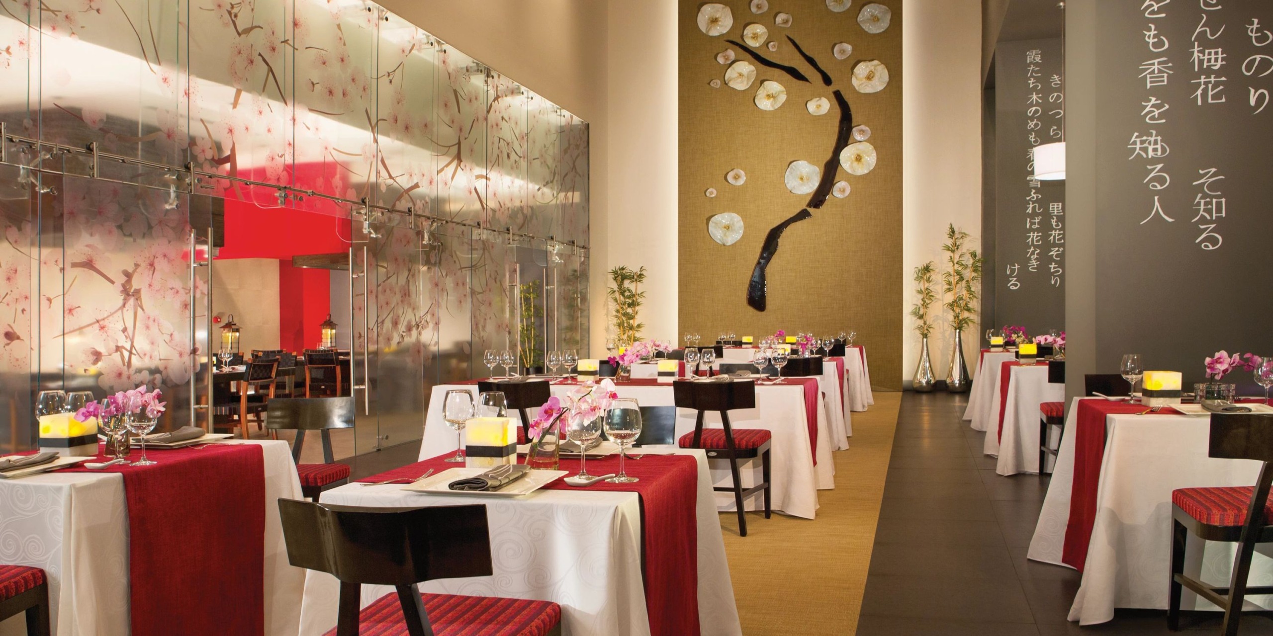 Dreams Vallarta Bay boasts an elegant dining area featuring red and white table settings, floral wall decor, and ambient lighting. Each table is adorned with flower arrangements and meticulously set dining places.