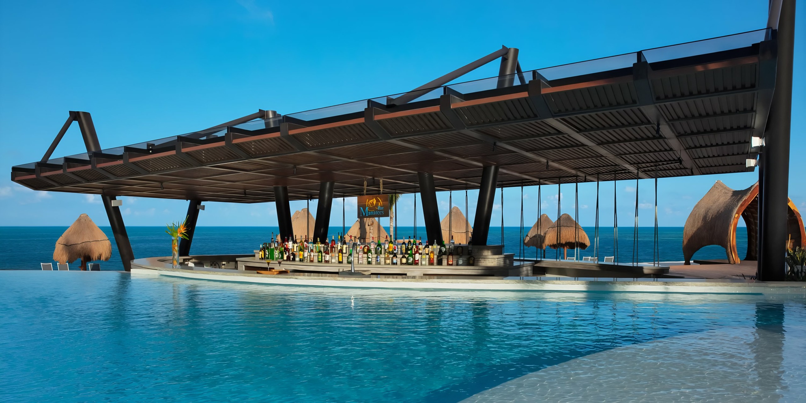 A modern Dreams Natura poolside bar with a shaded seating area overlooking the ocean.