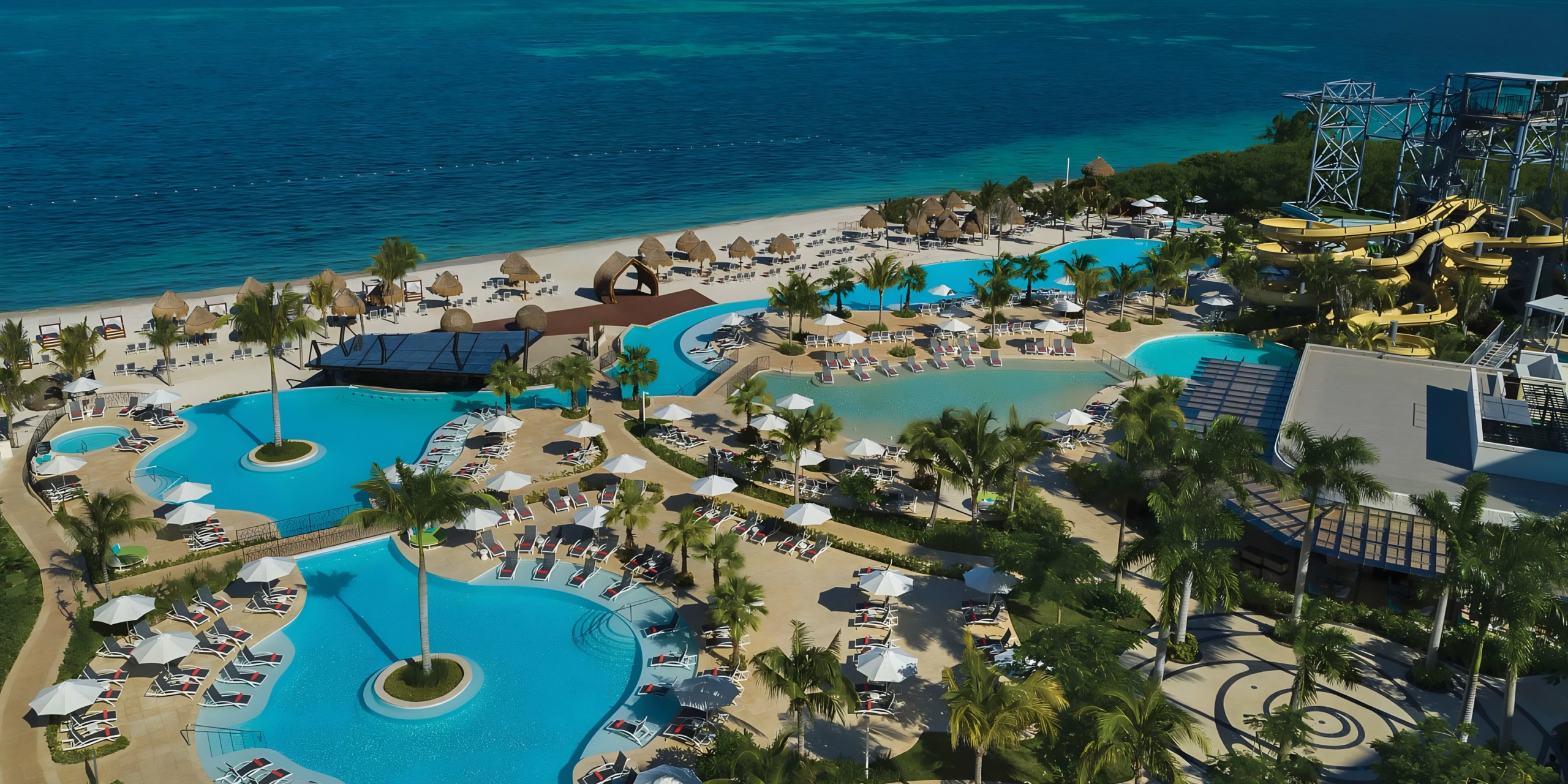 Aerial view of Dreams Natura tropical resort with swimming pools, water slides, and beachfront lounging areas.