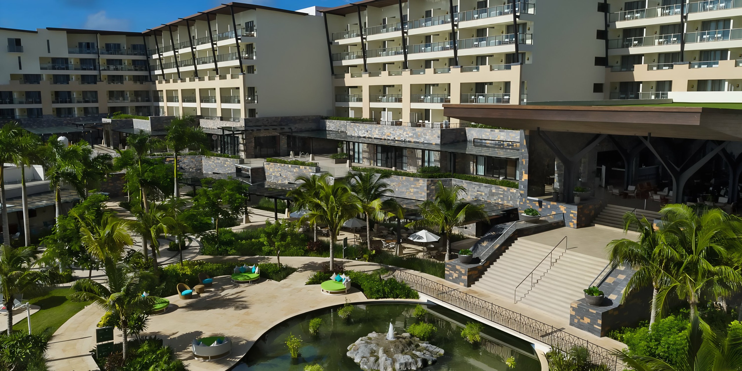 Modern resort with multiple buildings overlooking an outdoor seating area with a fountain and landscaping at Dreams Natura.