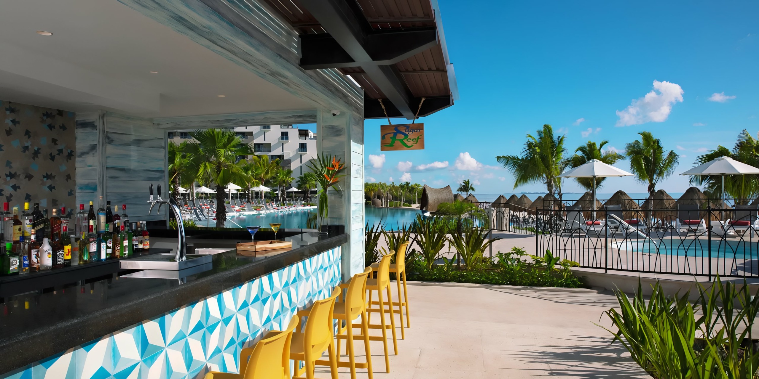Dreams Natura poolside bar with stools and a view of a tropical resort pool area.