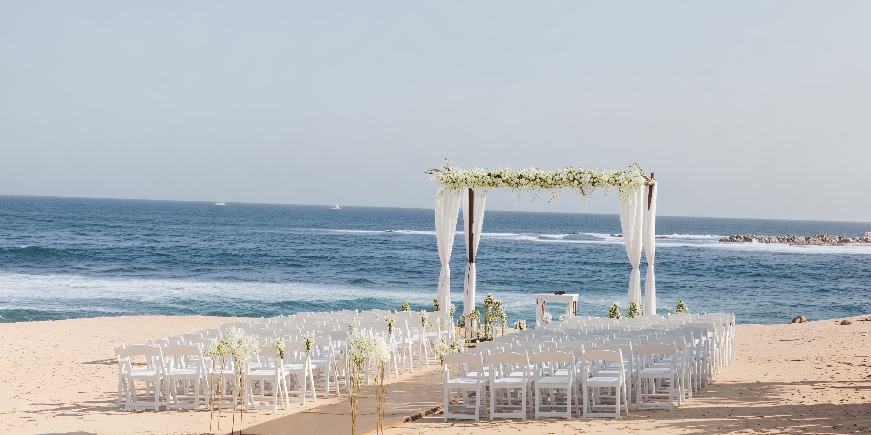 Wedding setup by the ocean at Grand Fiesta Americana Los Cabos, featuring chairs and a beautiful floral arch for a picturesque destination wedding.