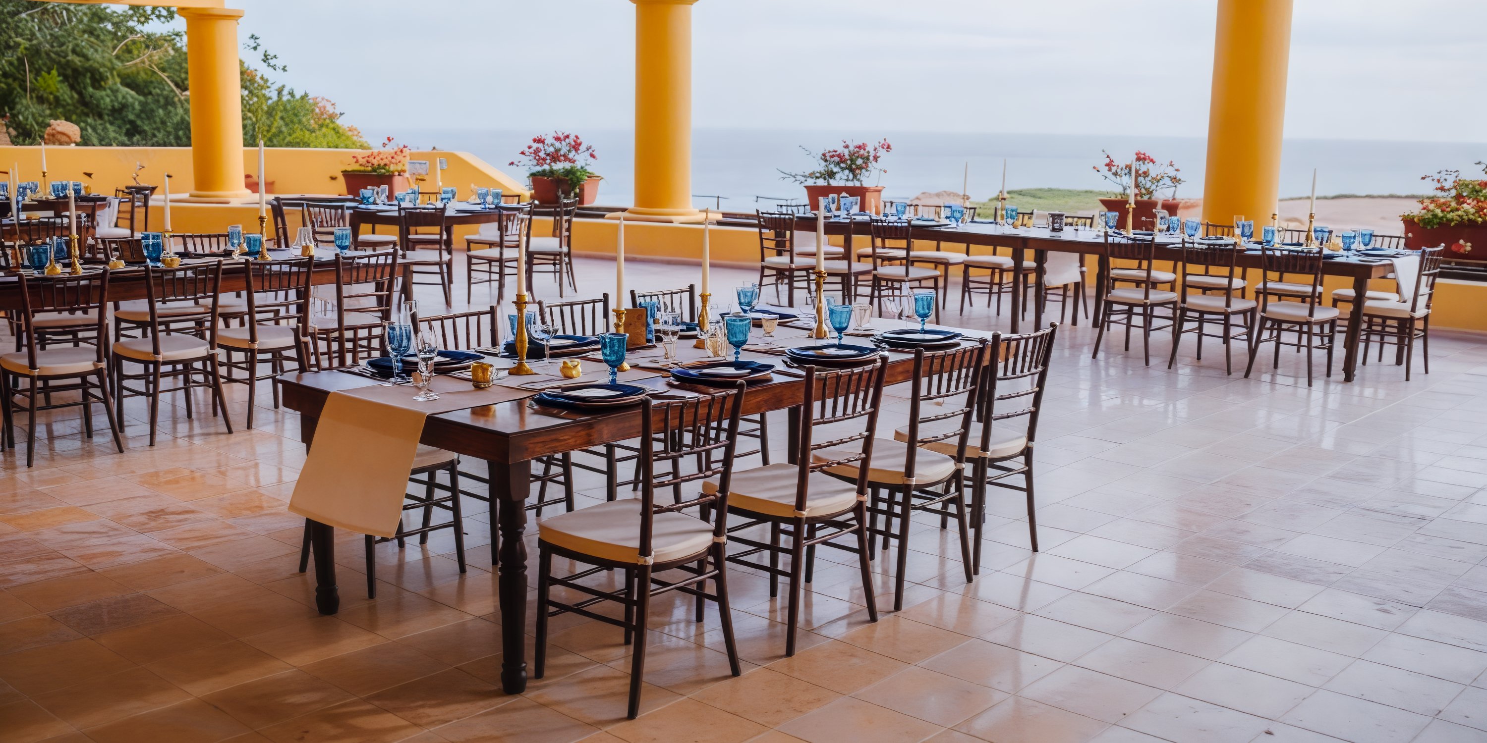 An enchanting outdoor dining area featuring wooden tables and blue plates, ideal for a destination wedding with a breathtaking sea view.