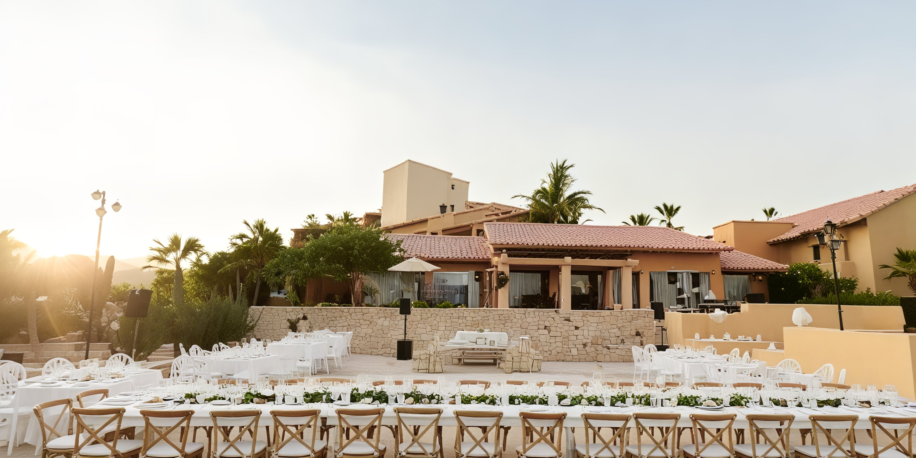 A breathtaking outdoor dining setup featuring long tables is elegantly arranged at Grand Fiesta Americana Los Cabos, creating the perfect setting for a destination wedding as the sun sets.