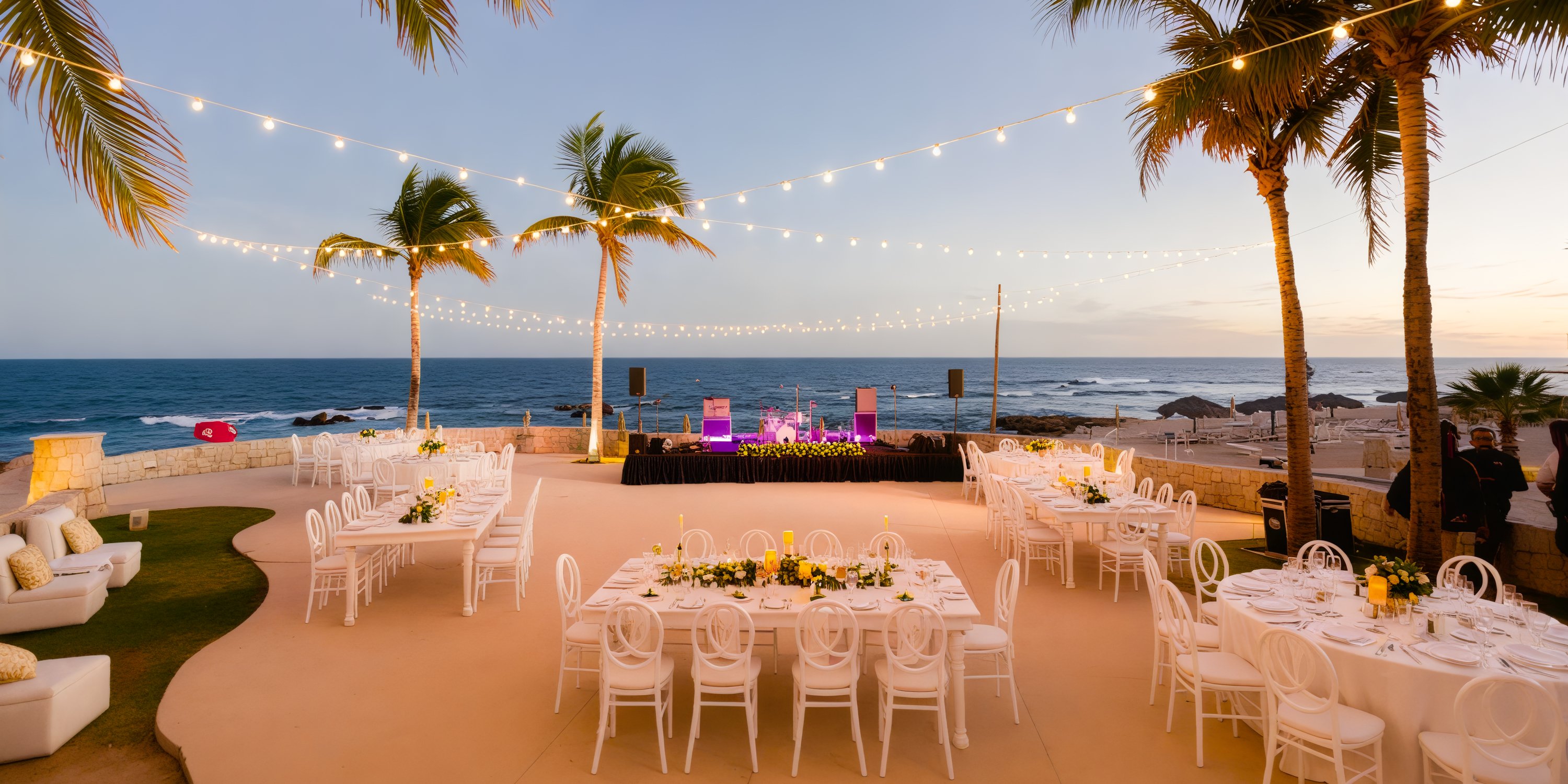 An enchanting destination wedding reception by the sea, featuring string lights illuminating tables and palm trees as the sun sets.