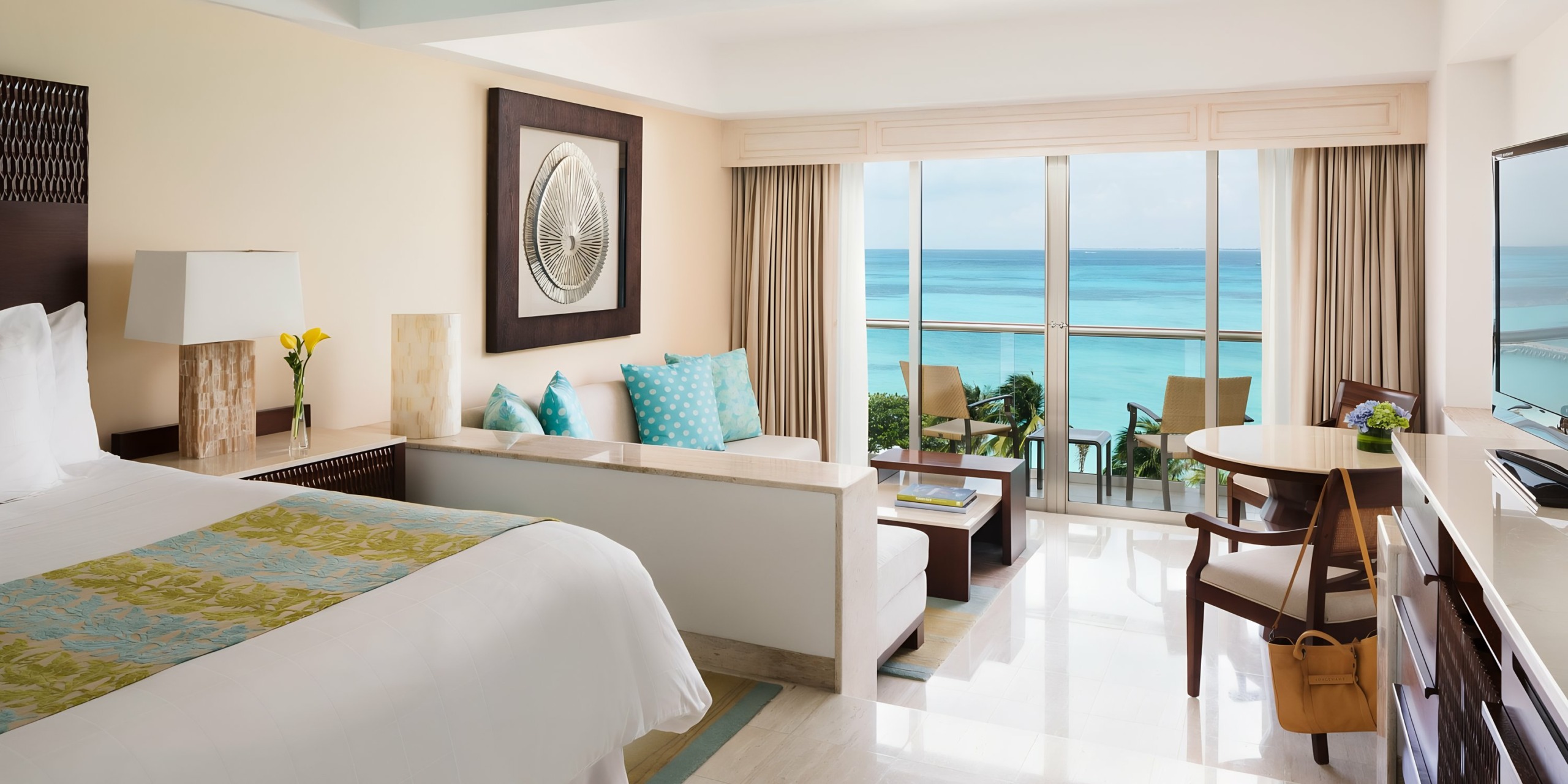 Grand Fiesta Americana Coral Beach hotel room with a large bed, desk, and a wide window overlooking a beach. Bright interior with ocean views.
