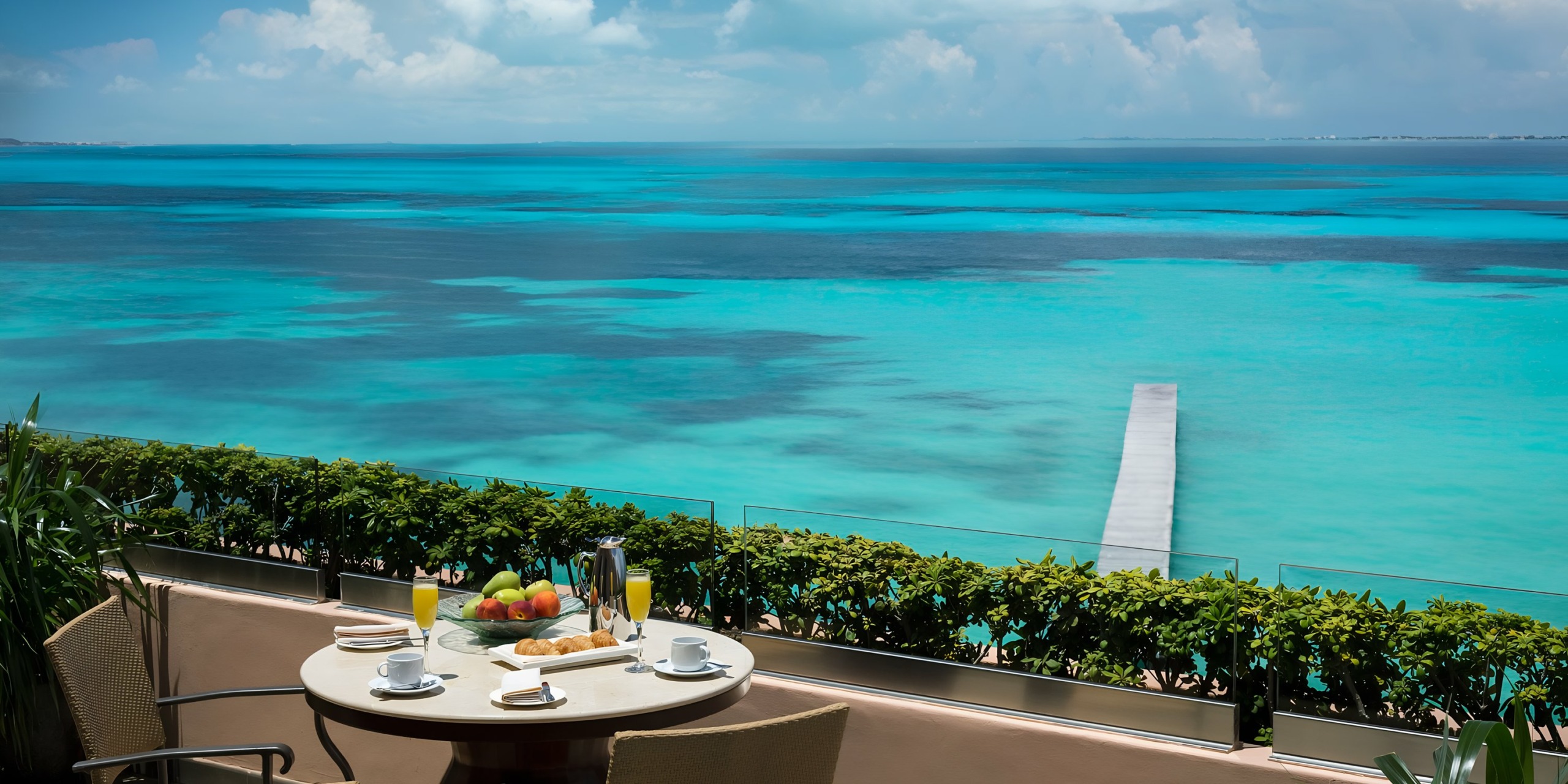 View from a Grand Fiesta Americana Coral Beach balcony overlooking a vibrant turquoise ocean, with a breakfast table set for two.