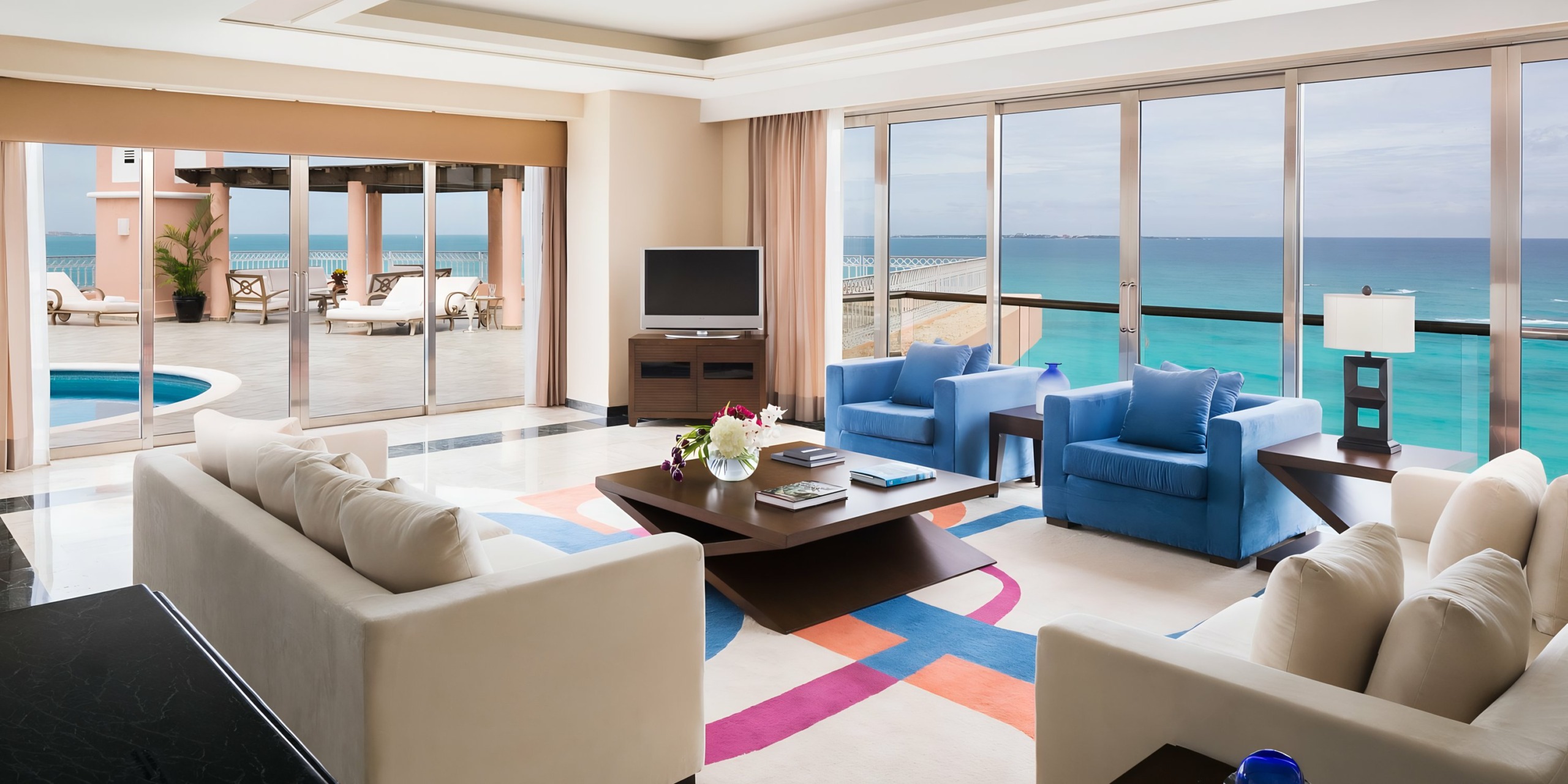 Luxurious beachfront Grand Fiesta Americana Coral Beach living room with open plan layout, large windows showcasing ocean views, and modern furniture including blue sofas and a black coffee table.