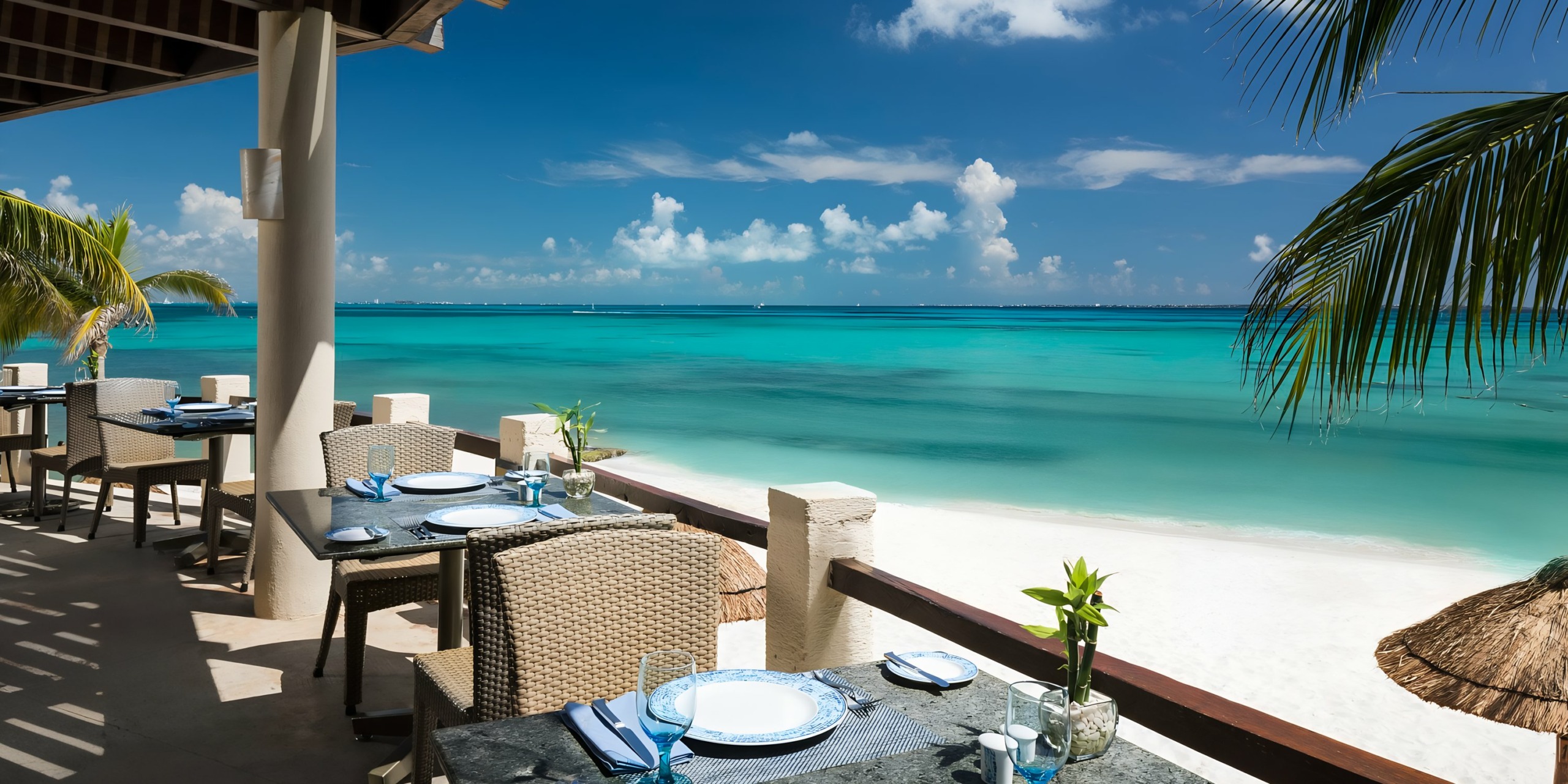 Seaside restaurant terrace at Grand Fiesta Americana Coral Beach with tables set for dining, overlooking a tranquil blue ocean under a clear sky.