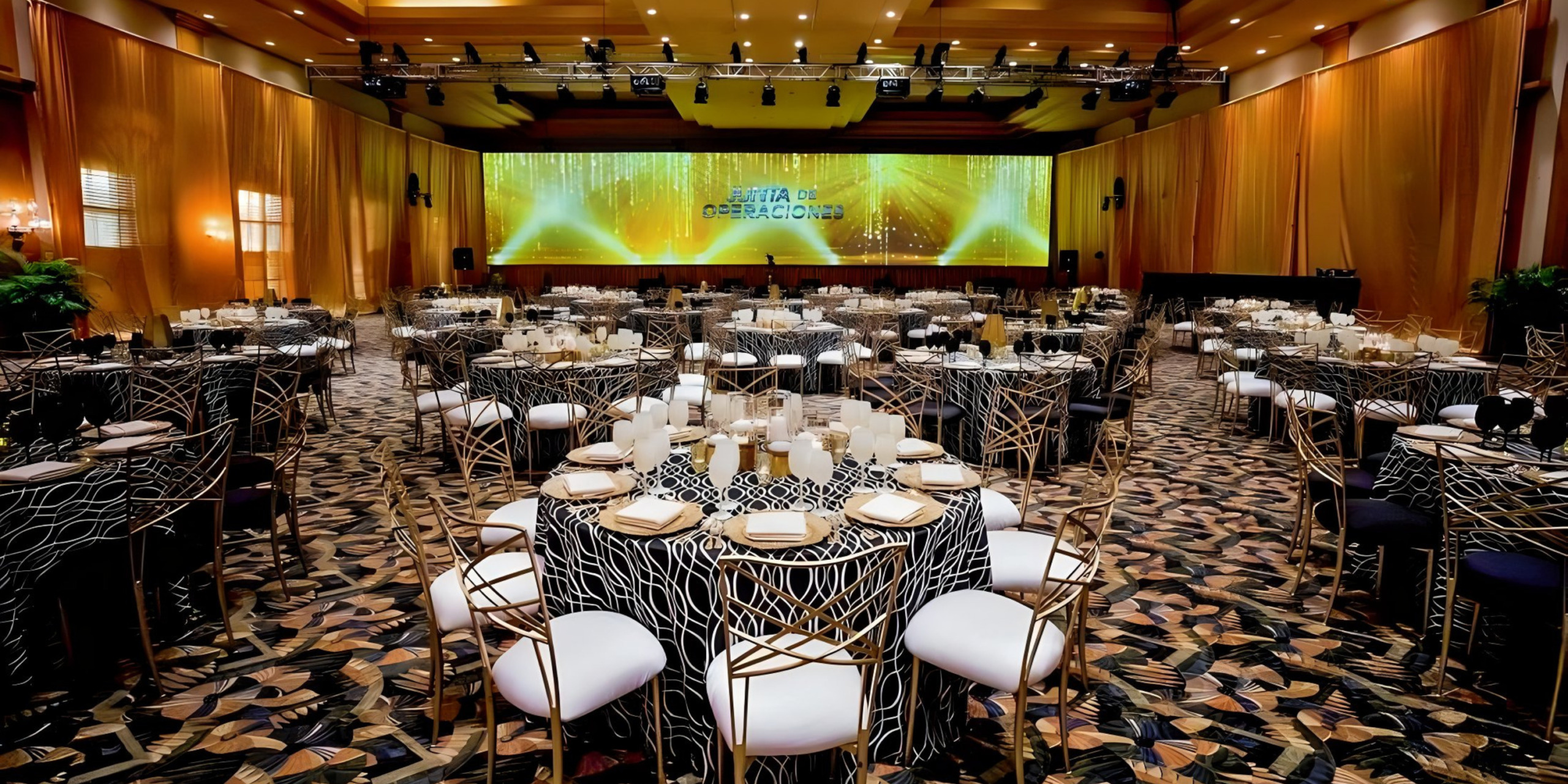 Elegant banquet hall setup with round tables, black and white chairs, and a stage displaying a green-themed "destination weddings" presentation.