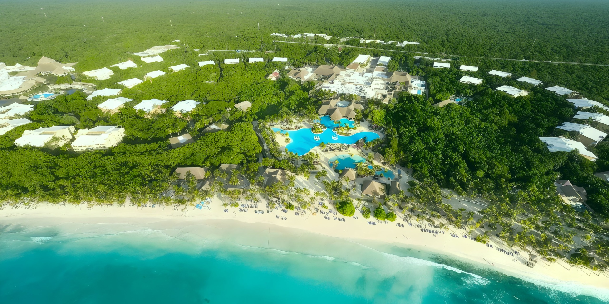 An aerial view of the Grand Palladium Kantenah resort reveals multiple swimming pools nestled amidst lush greenery, with a stunning white sand beach and turquoise ocean just beyond.