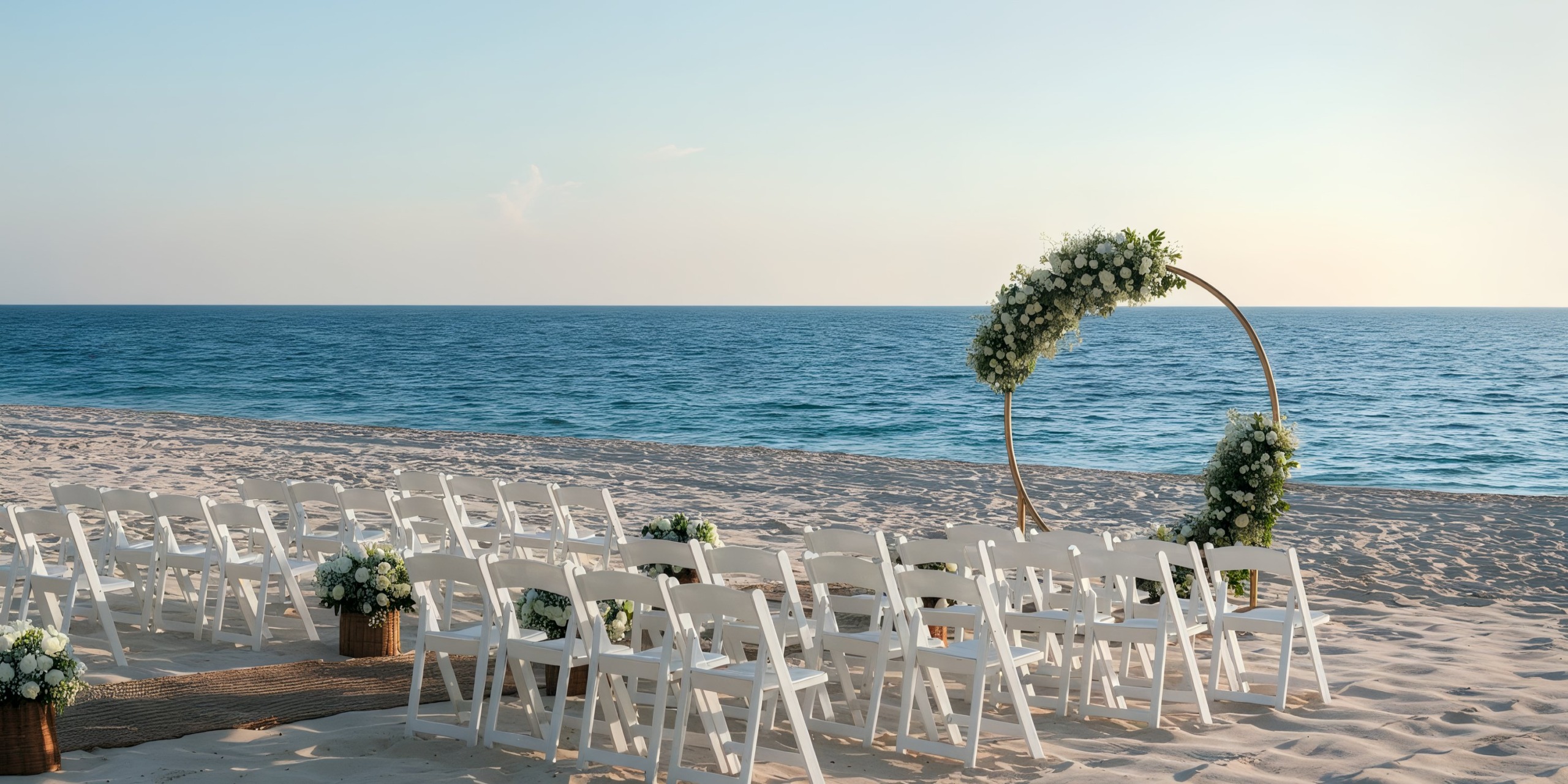 A beach wedding setup at the Grand Palladium Kantenah featuring white chairs arranged in rows and a circular floral arch overlooking the ocean.