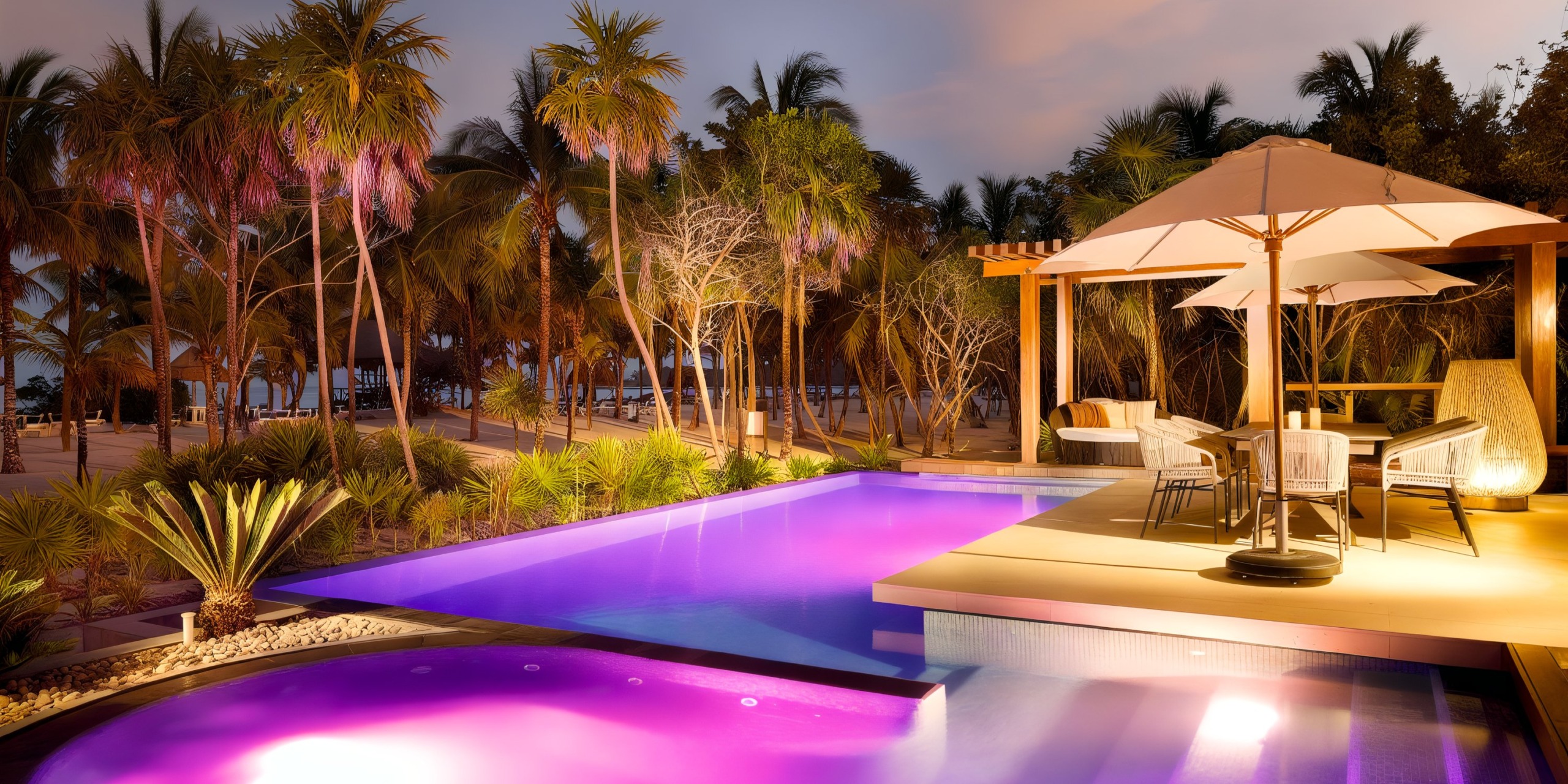 As the sun sets, the Grand Palladium Kantenah offers a contemporary outdoor pool area where glowing purple water is encircled by palm trees, cozy seating beneath umbrellas, and scenic views of a distant beach.