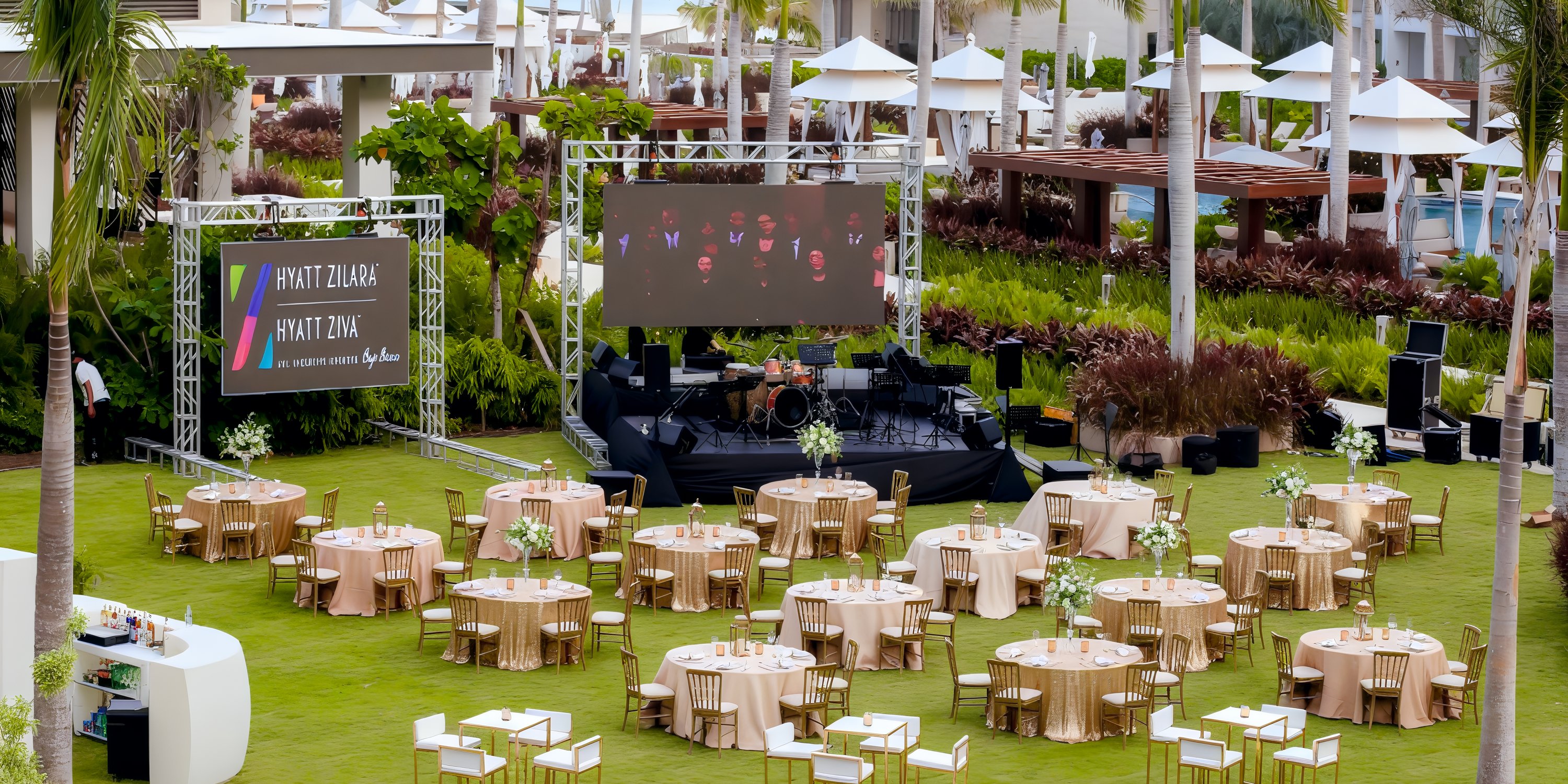 Hyatt Zilara Cap Cana destination wedding setup with round tables, chairs, stage, and large screens on lawn.