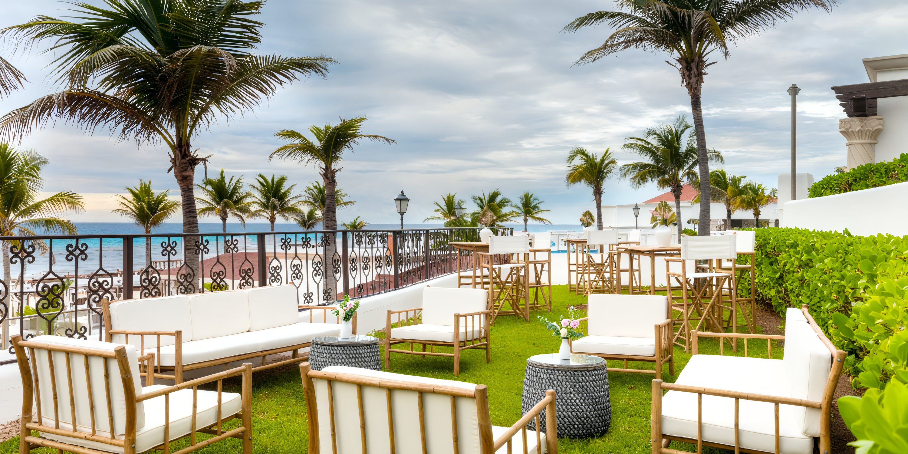 At Hyatt Zilara Cancun, envision your destination wedding amidst white chairs and tables elegantly arranged for guests, with an ocean view under swaying palm trees in the exquisite outdoor seating area.