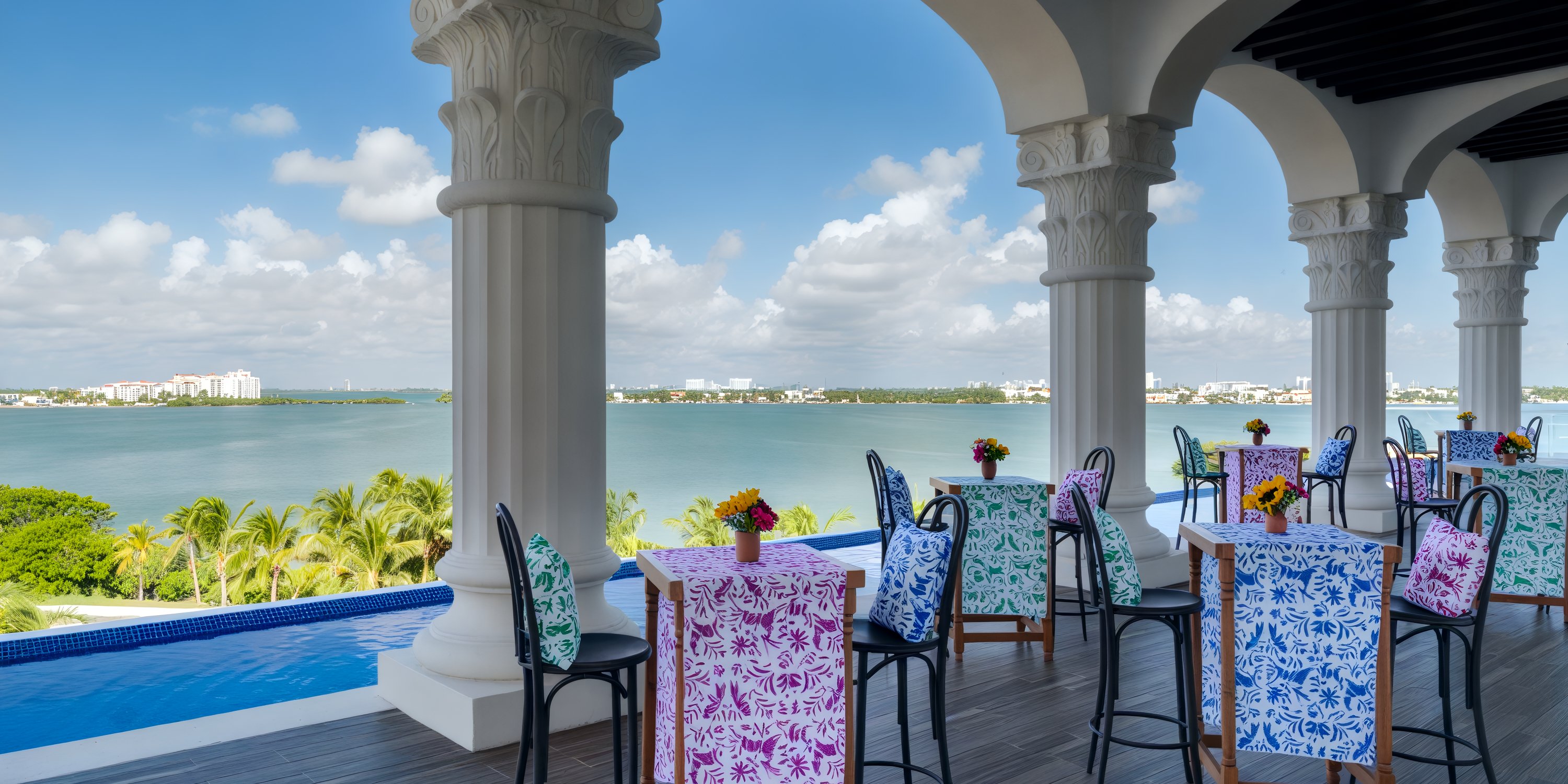 Hyatt Zilara Cancun terrace offers a stunning backdrop for a destination wedding, featuring colorful tables, a serene water view, and a distant cityscape.