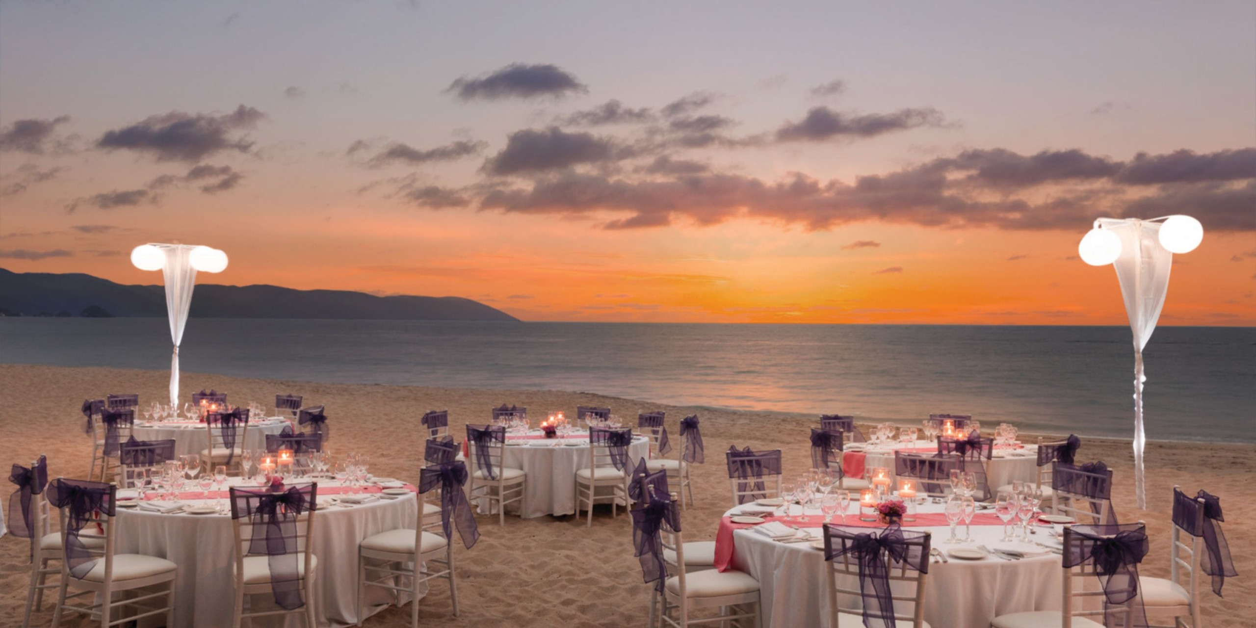 Hyatt Ziva Puerto Vallarta offers a breathtaking destination wedding at sunset, featuring elegantly decorated tables and chairs on the beach.