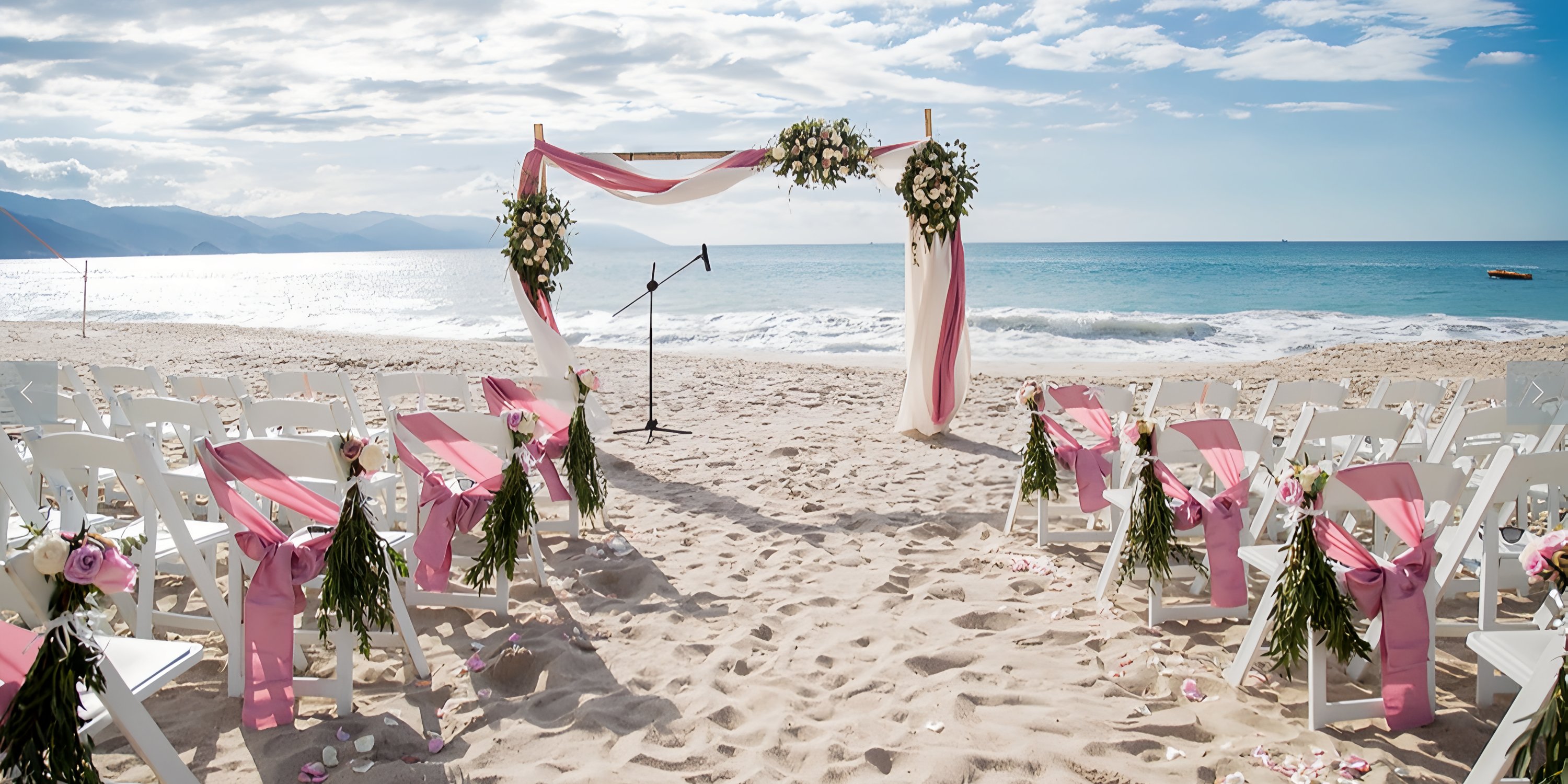 White chairs with pink sashes face a floral arch at a destination wedding in Hyatt Ziva Puerto Vallarta.