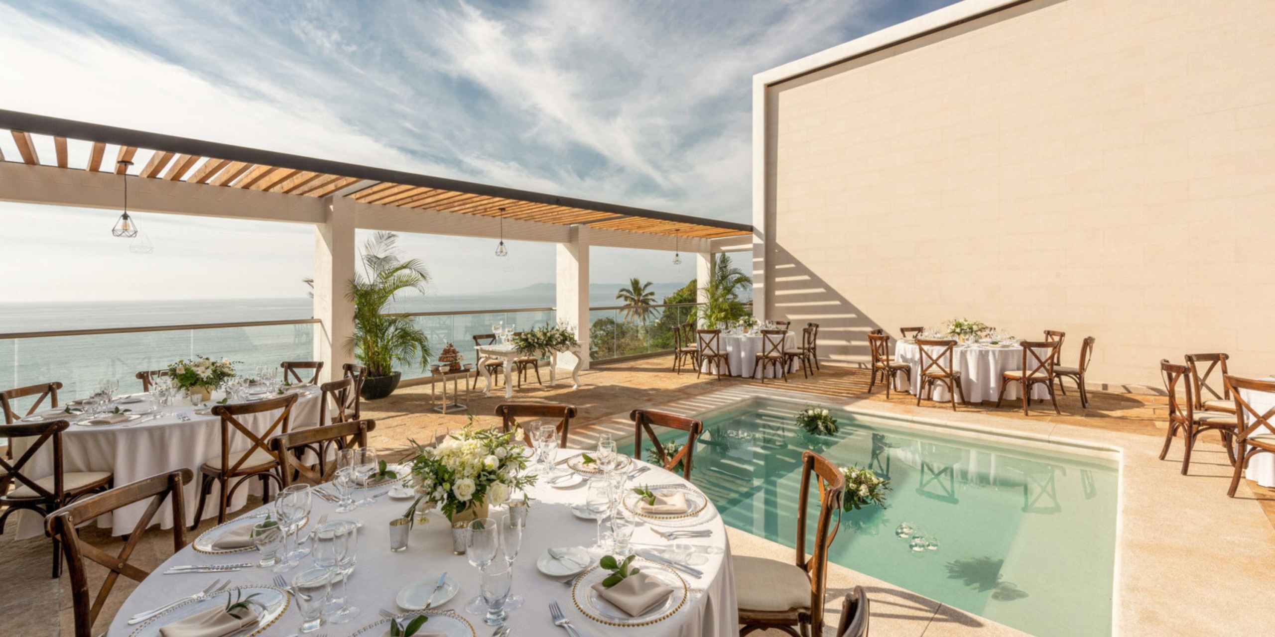 Seaside destination wedding reception arranged with elegantly set tables and a charming small pool nearby.