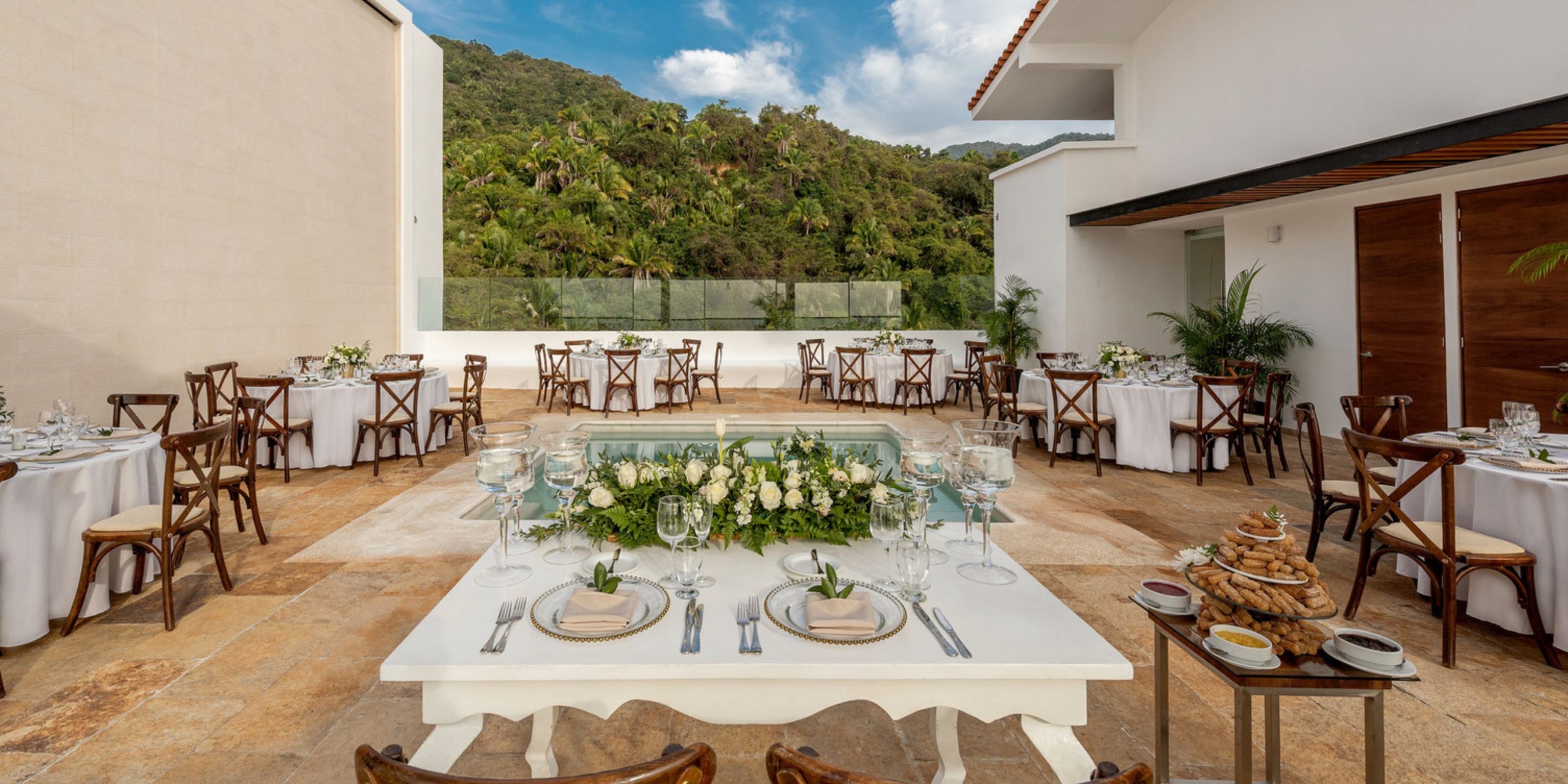 An outdoor destination wedding reception featuring elegantly arranged tables, all set against a stunning mountain backdrop.