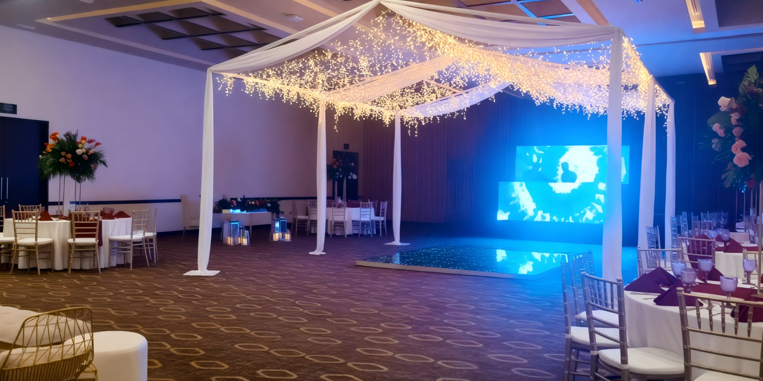 Hyatt Ziva Riviera Cancun's event hall, perfect for a destination wedding, is beautifully adorned with an elegant canopy, tastefully arranged tables, and a large screen to enhance the celebration.