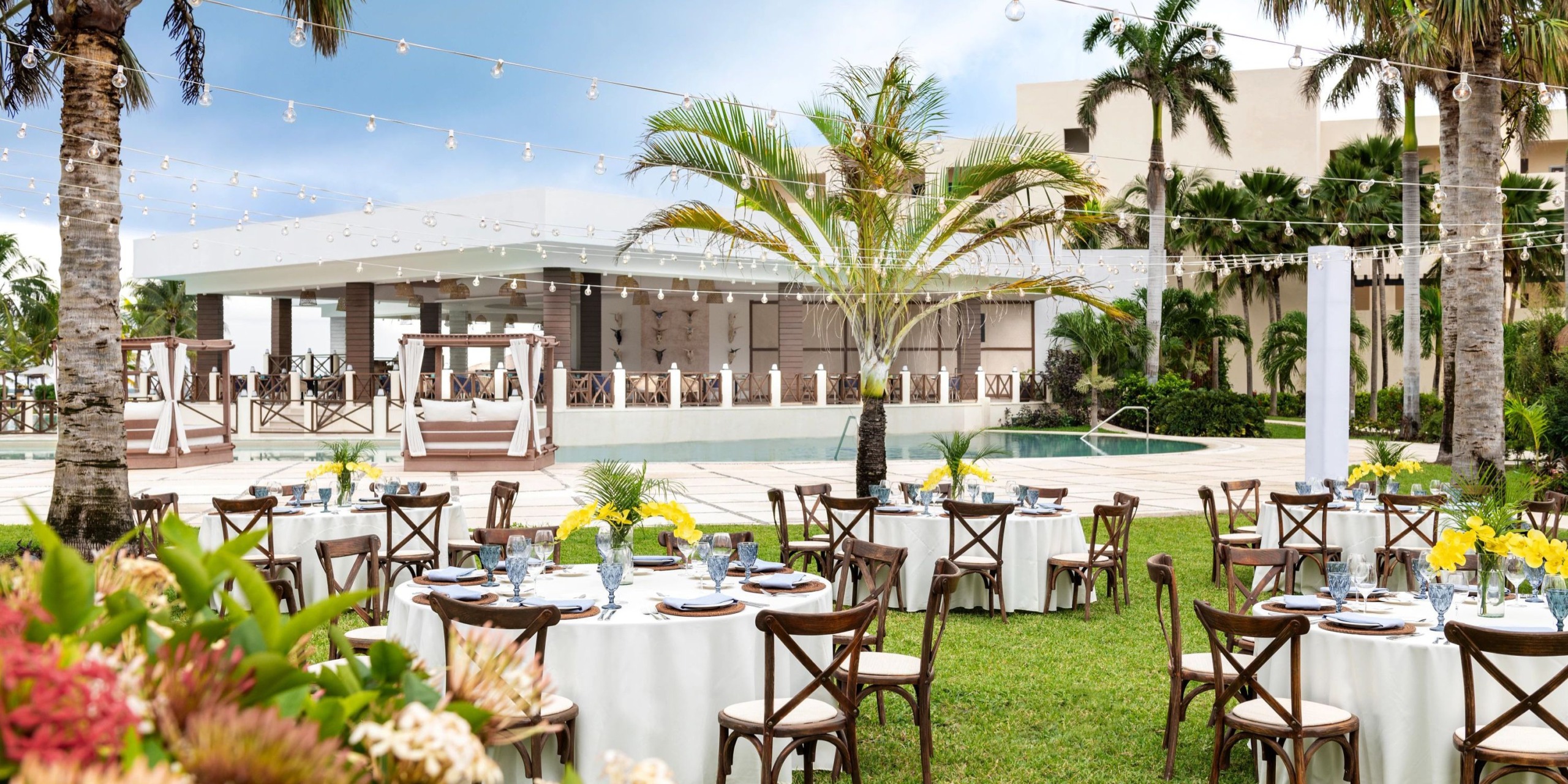 Experience the enchanting destination wedding at Hyatt Ziva Riviera Cancun, featuring elegantly set tables and chairs adorned with string lights and lush greenery for a picturesque outdoor ceremony.