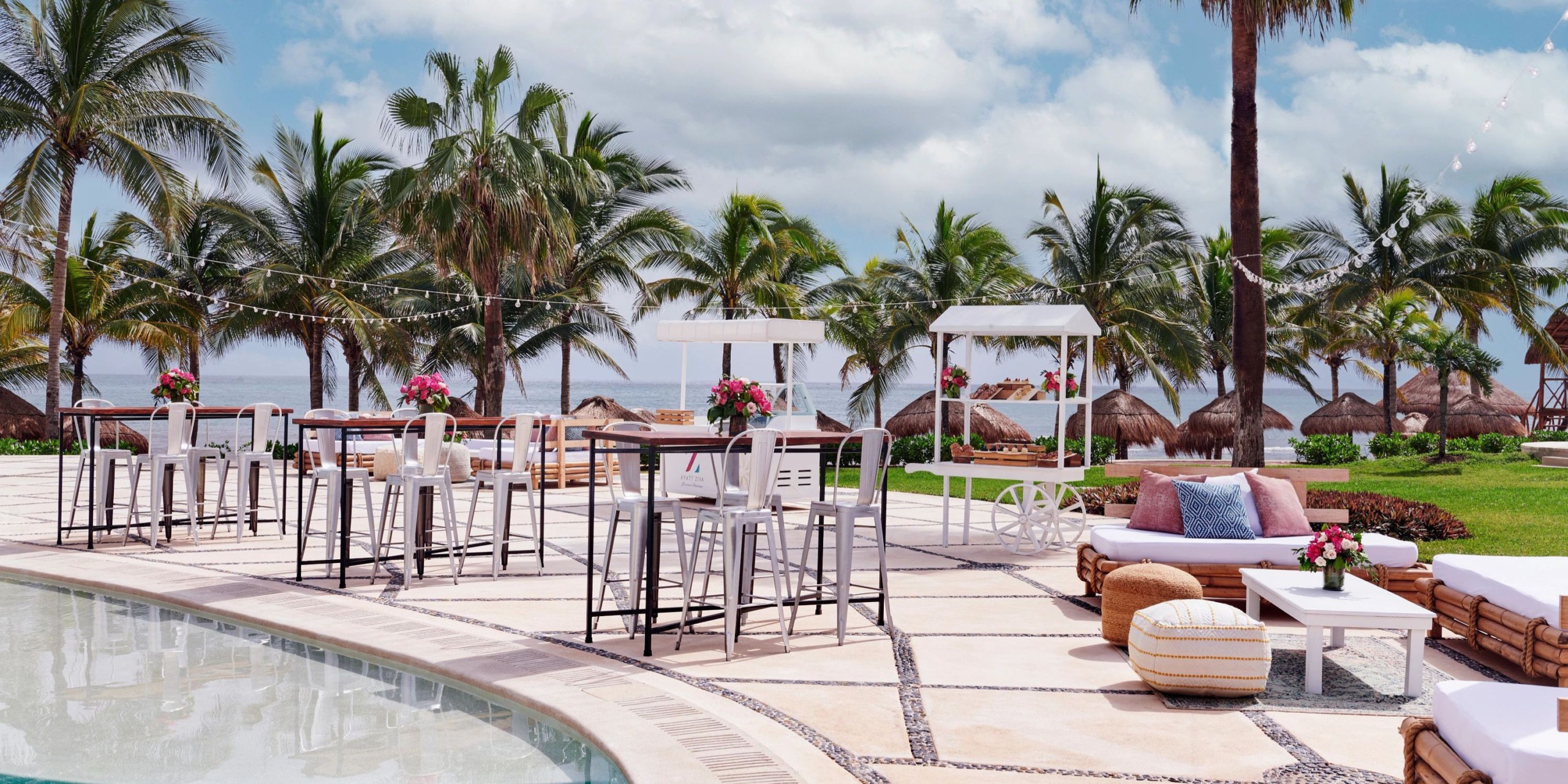 Hyatt Ziva Riviera Cancun's patio, adorned with bar tables and palm trees, provides a stunning backdrop for a destination wedding, complete with an ocean view under the clouds.