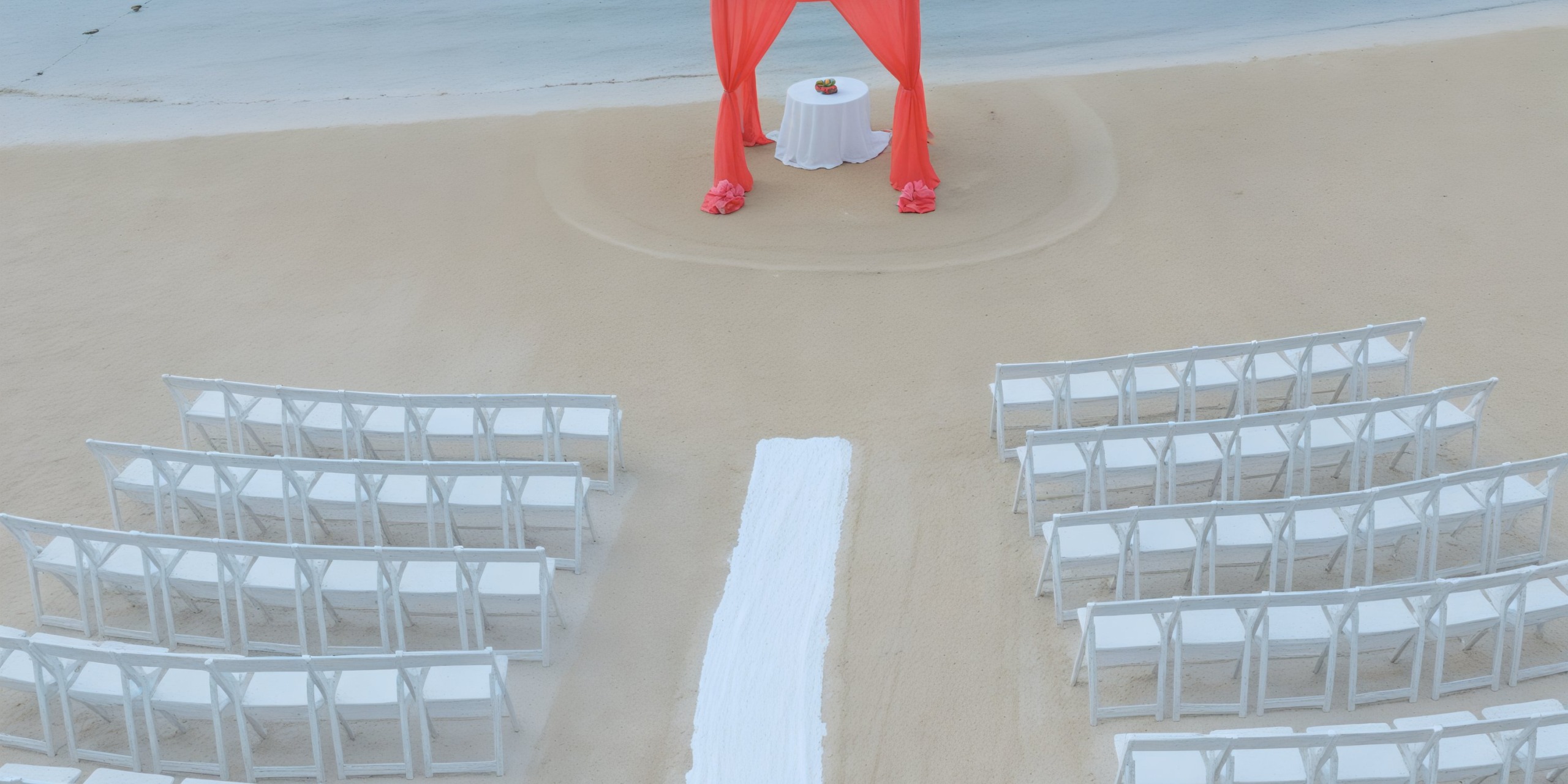A stunning destination wedding setup featuring white chairs and a vibrant red arch awaits at the Hideaway at Royalton Blue Waters.