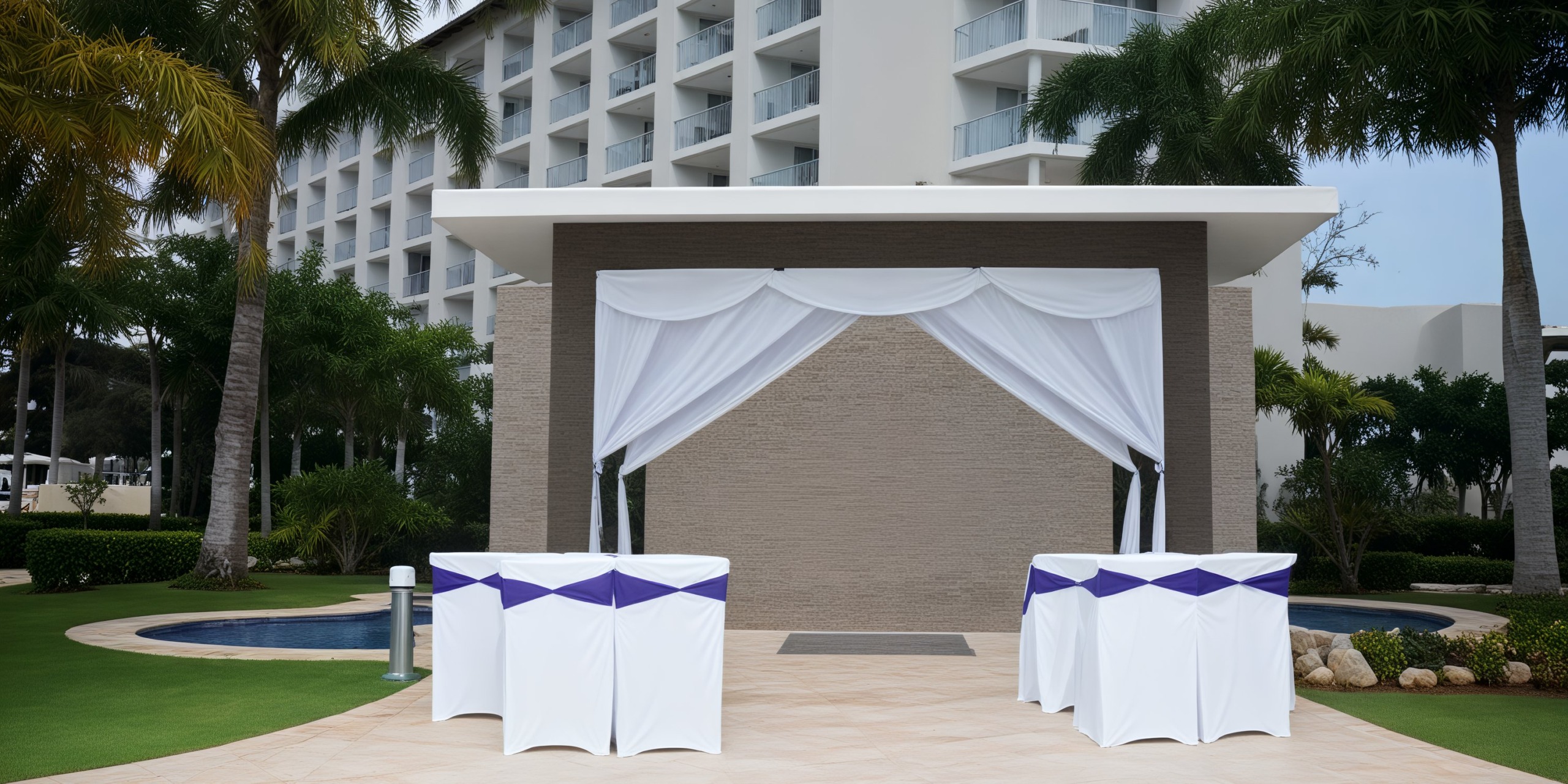 Hideaway at Royalton Blue Waters offers a stunning outdoor altar adorned with elegant white drapes, perfect for a picturesque destination wedding. The setting is beautifully complemented by tables dressed in white and purple cloths, creating an exquisite backdrop for your special day.