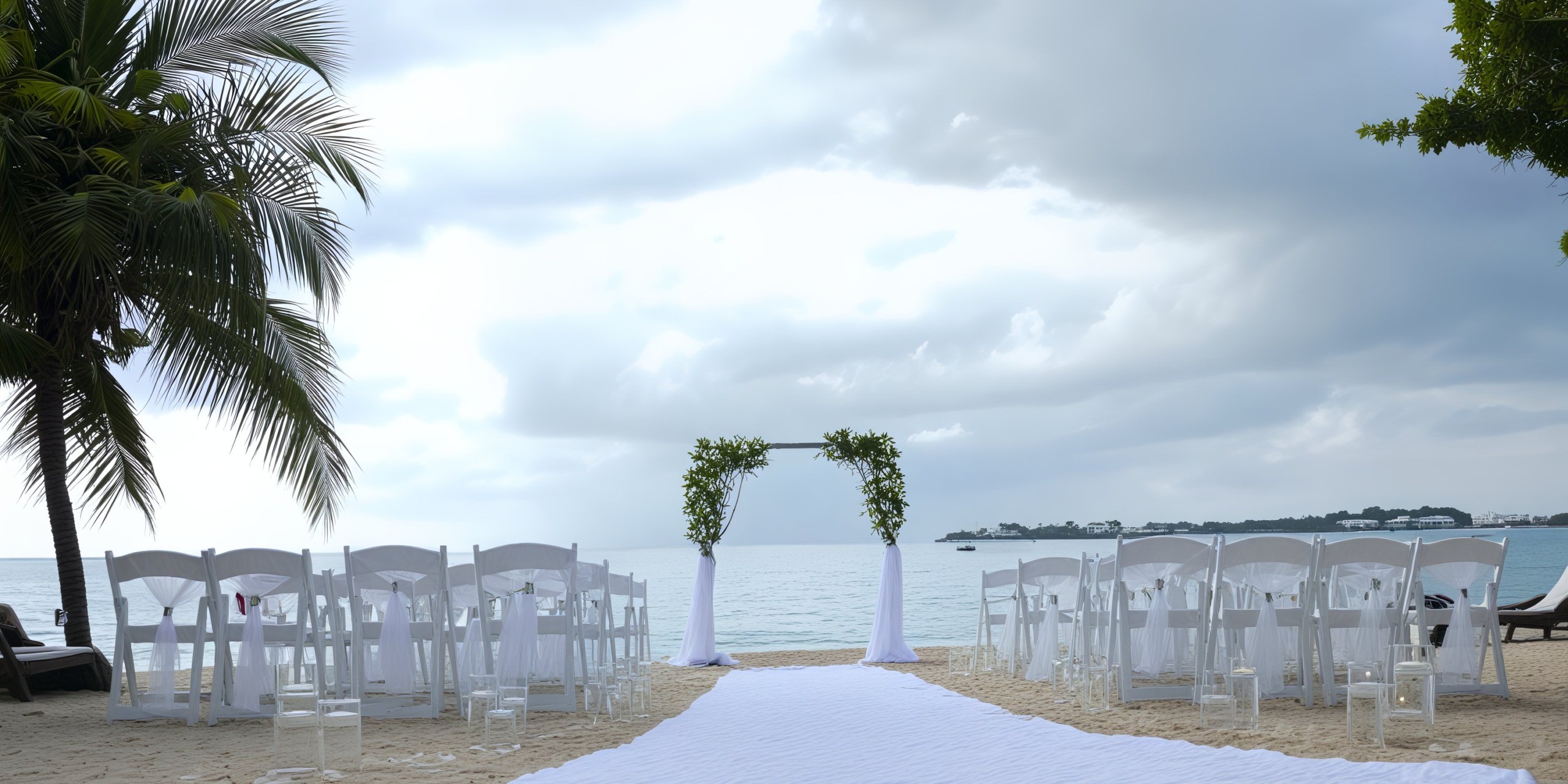 Destination wedding arranged at Hideaway at Royalton Negril features a stunning setup with chairs lining the aisle, a beautifully adorned arch, and a picturesque palm tree enhancing the romantic beach ambiance.